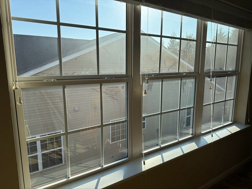 A three-pane window with grids, looking out at a tan-sided building under a bright blue sky.