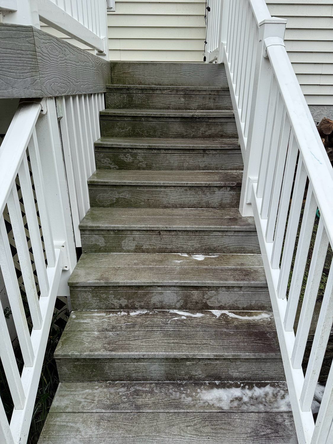 Weathered wooden outdoor stairs with white railings lead up to a house entrance.