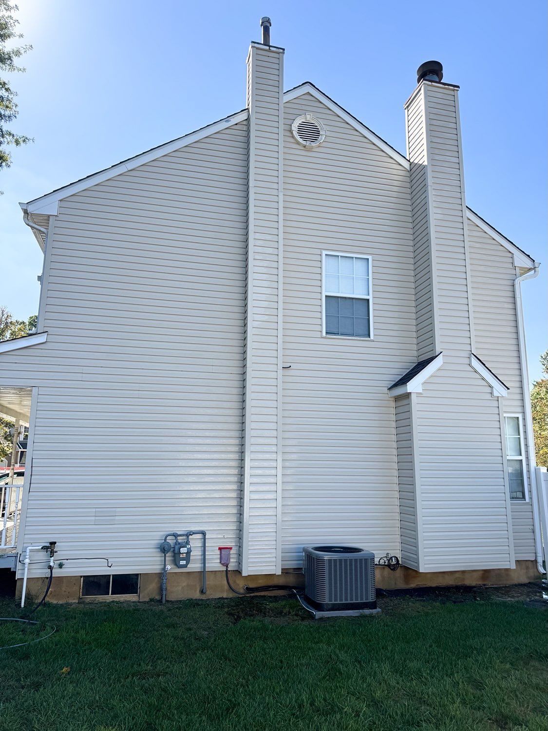 Side view of a two-story beige house with two exterior chimneys, a central window, and an air conditioning unit.