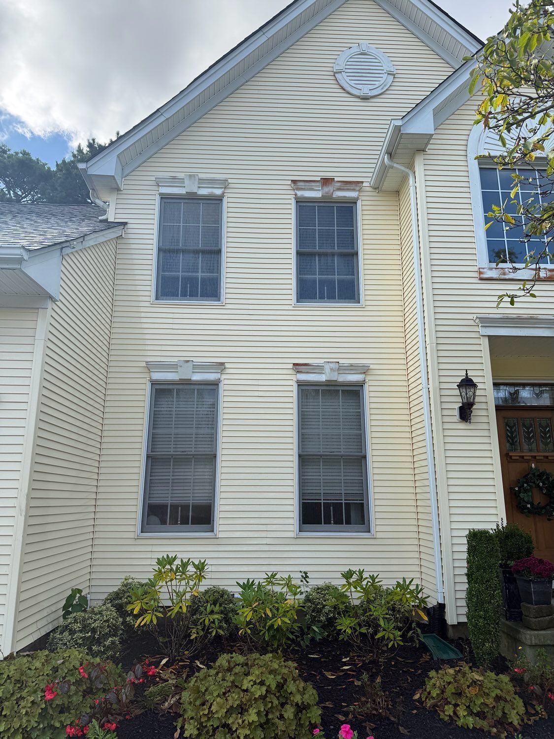 A light yellow house exterior with vinyl siding and four double-hung windows above a garden bed.