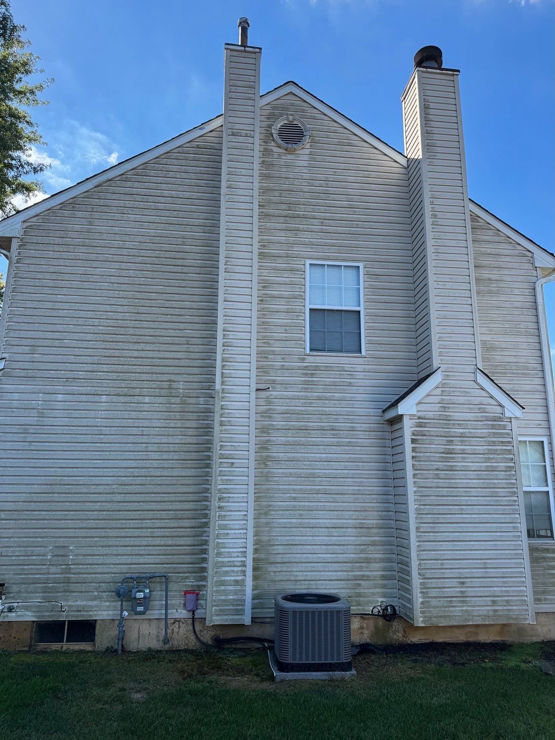 Two chimneys on a side wall of a two-story house with light-colored siding featuring dark horizontal streaks of grime.