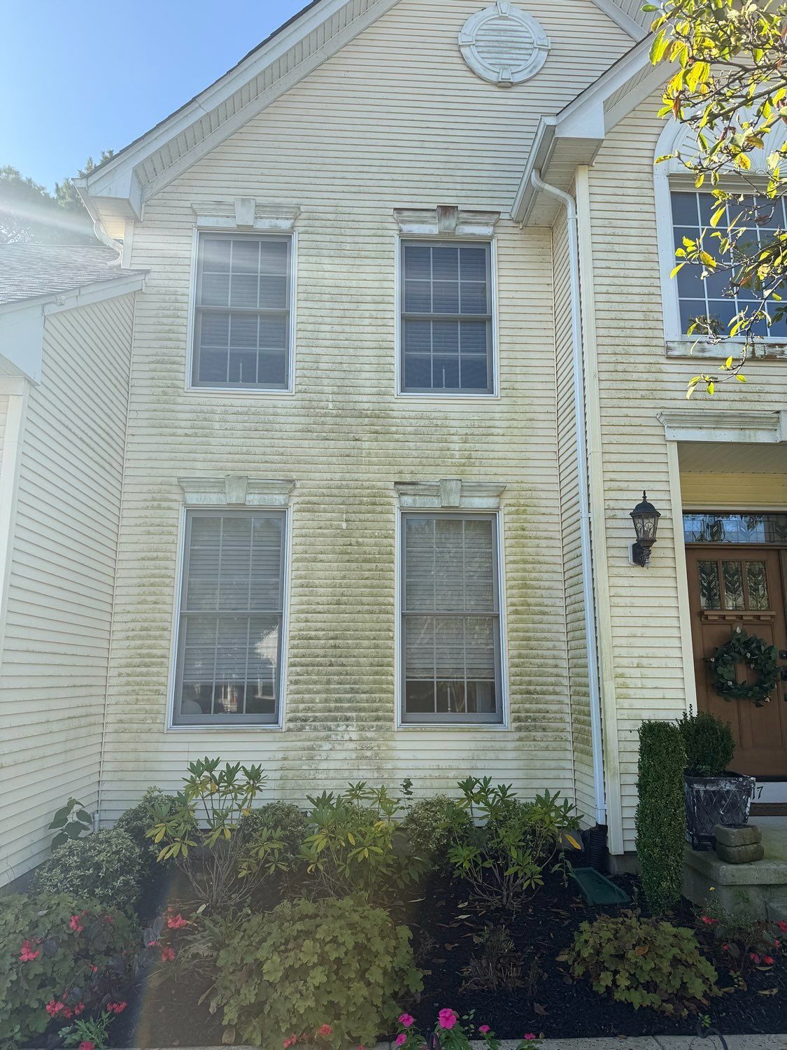 A two-story house with cream siding showing significant mold or mildew growth, particularly between the windows.