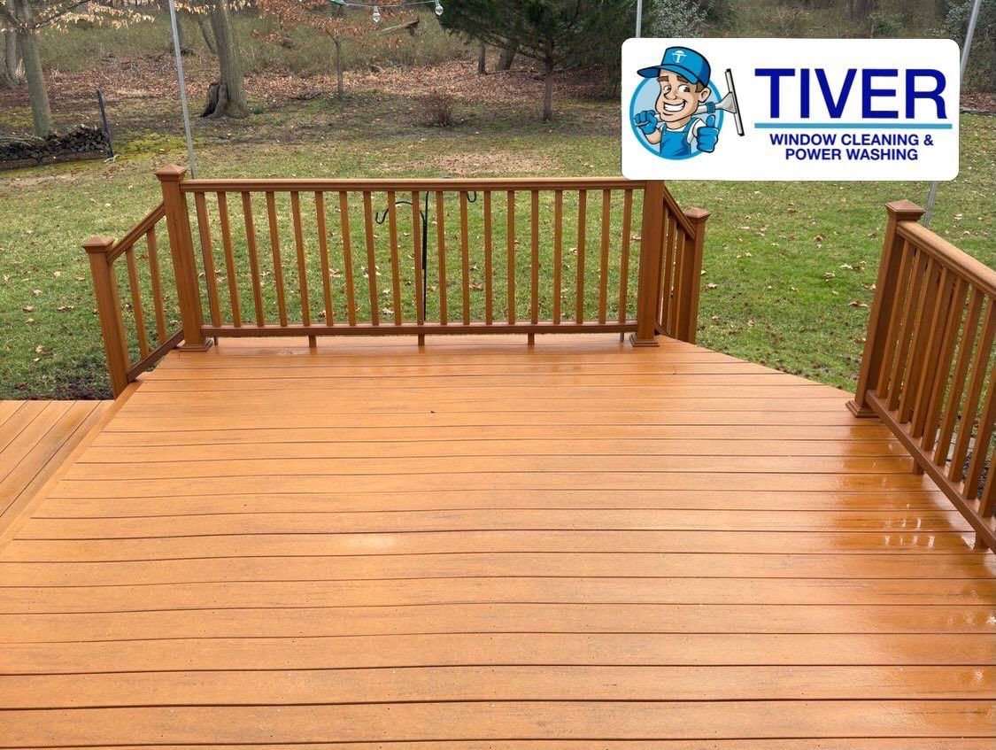A wooden deck with a railing overlooks a grassy backyard, featuring a Tiver Window Cleaning & Power Washing company logo.