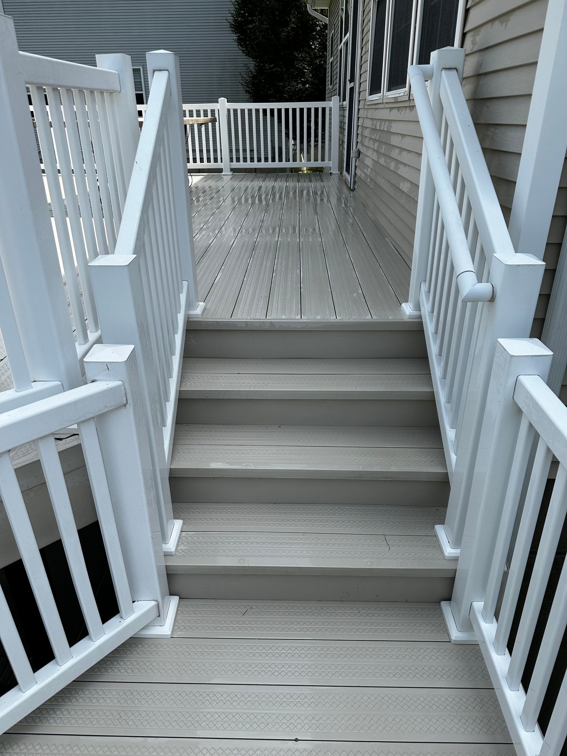 A set of grey composite deck stairs with white railings leading up to a raised deck platform.