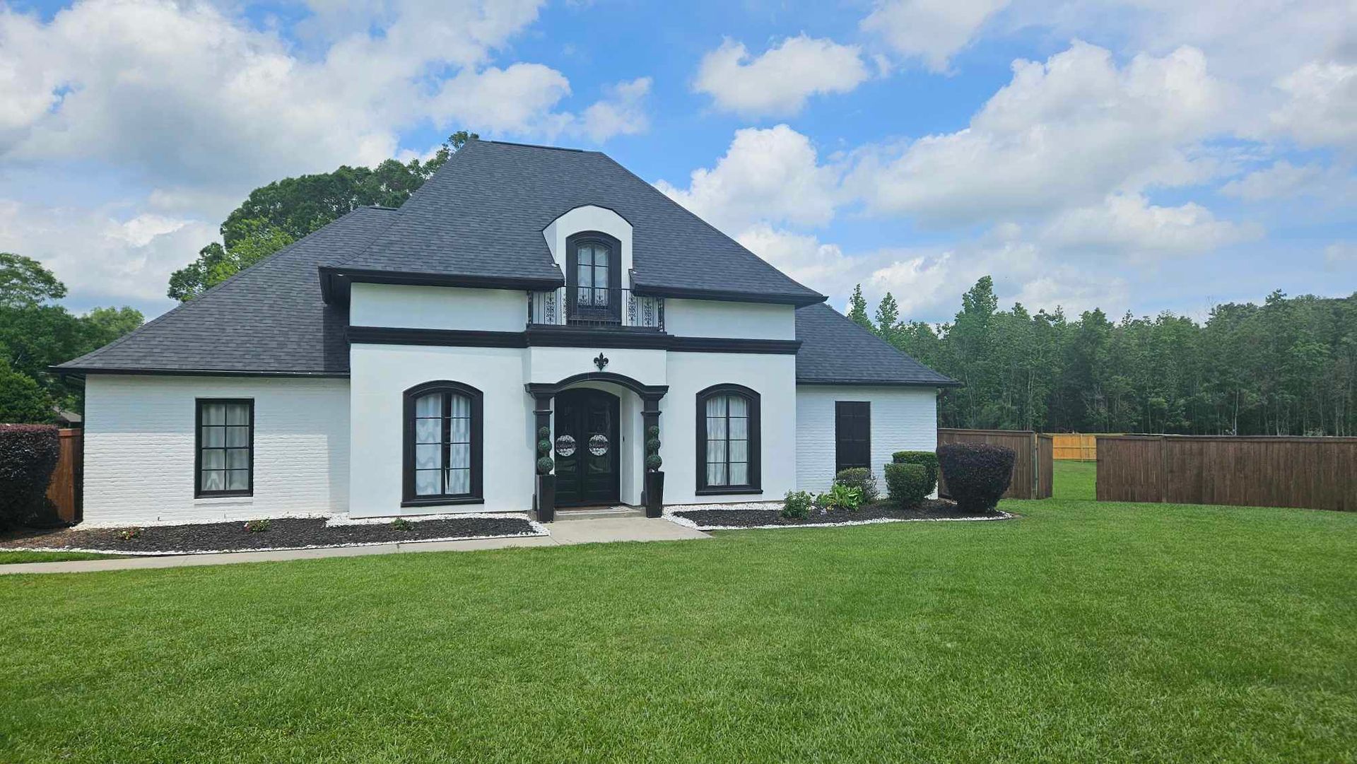 A large white house with a black roof is sitting on top of a lush green field.