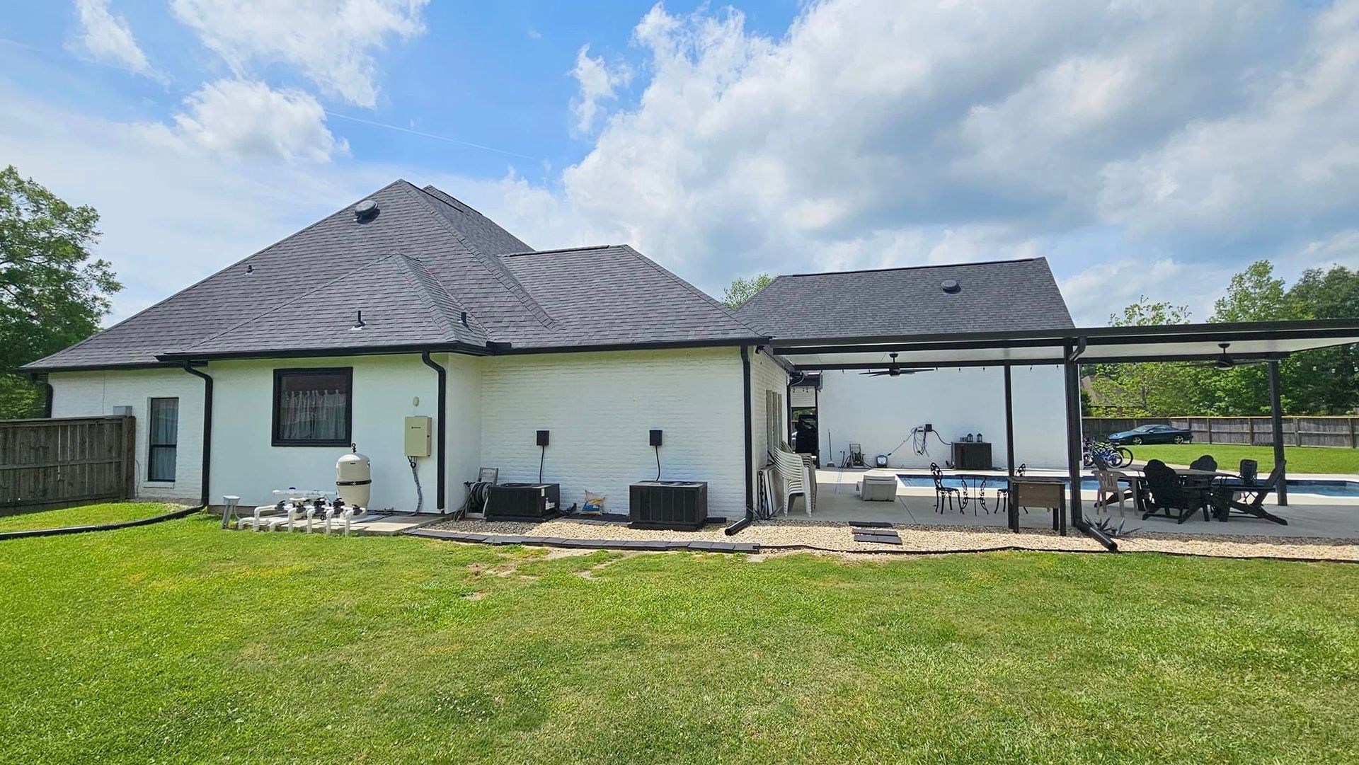 A white house with a black roof and a covered patio in the backyard.