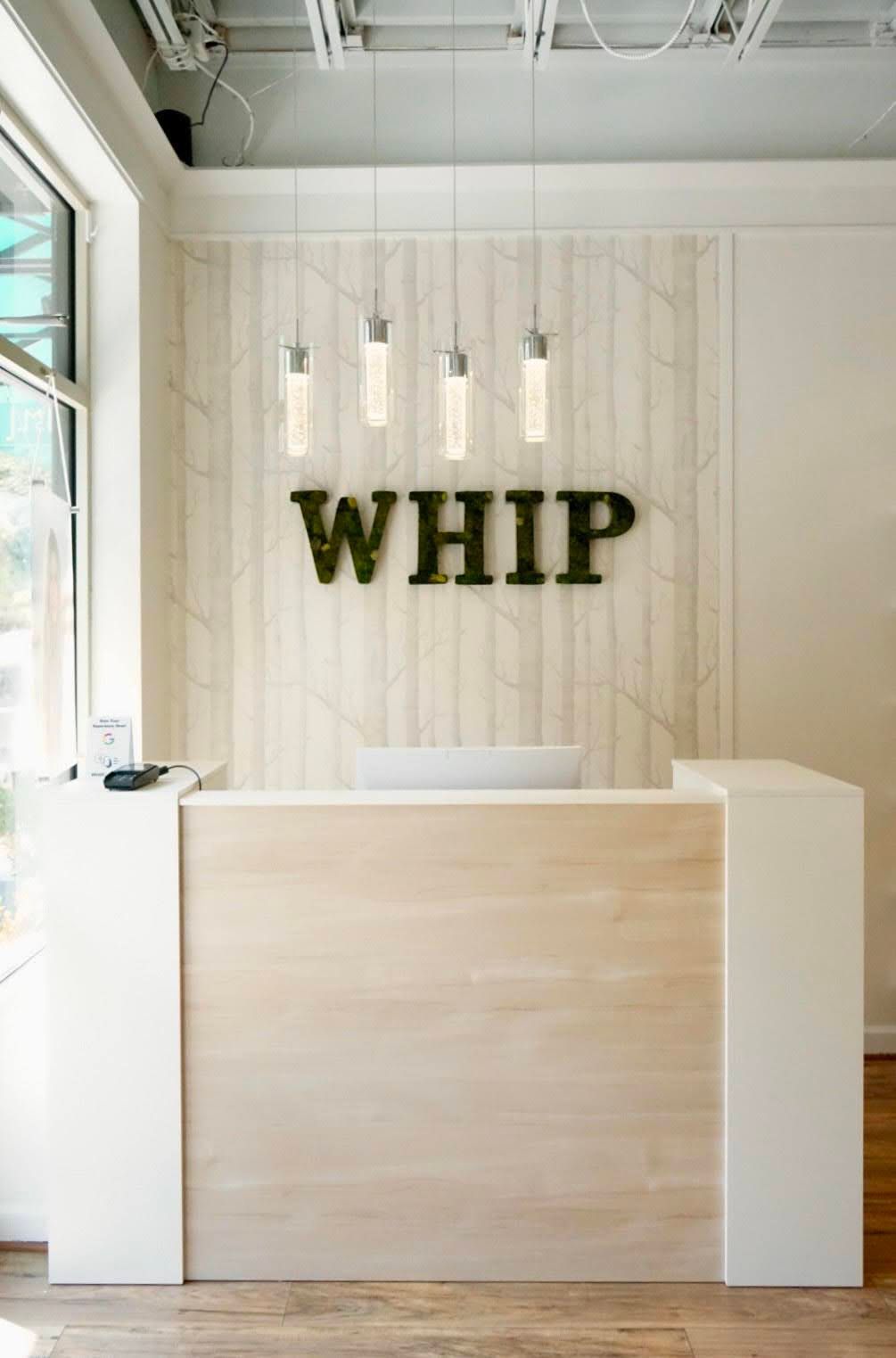 A reception desk in a store with the word whip on the wall.
