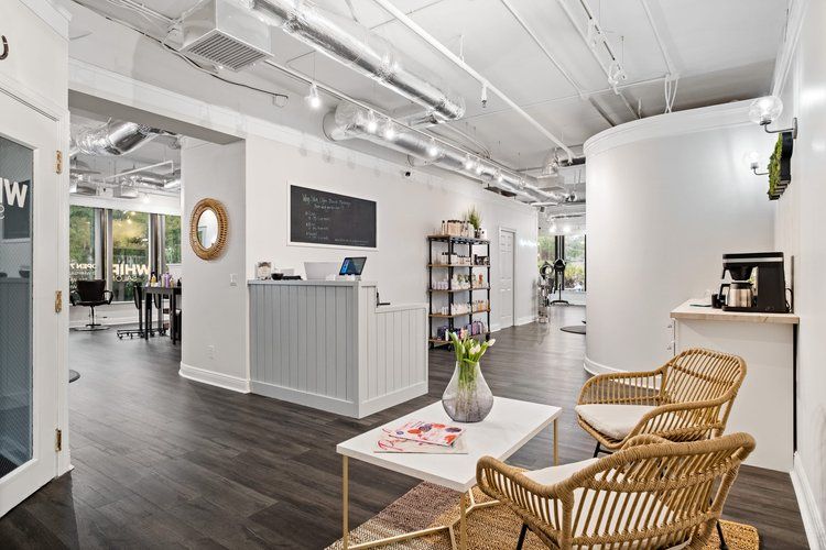 A salon with a reception desk , chairs , a table and a vase of flowers.