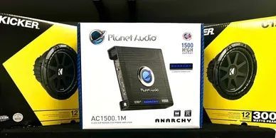 A kicker amplifier is sitting on top of a shelf next to a pair of speakers.