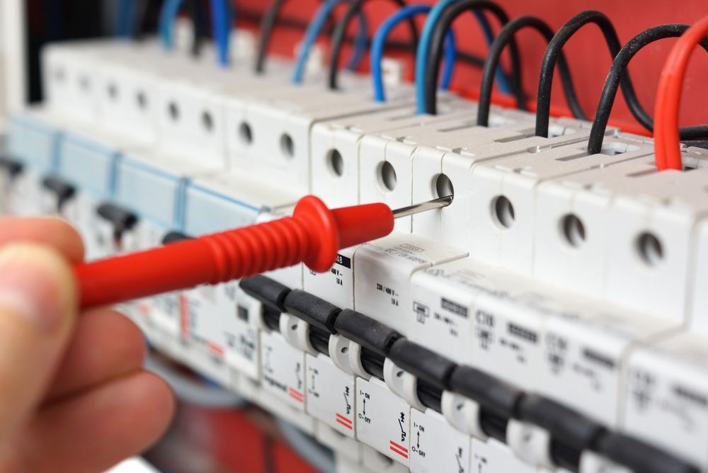 A hand holds a red multimeter probe against the electrical terminal of a circuit breaker in a distribution board — Milton Electrical Projects In Kaban, QLD