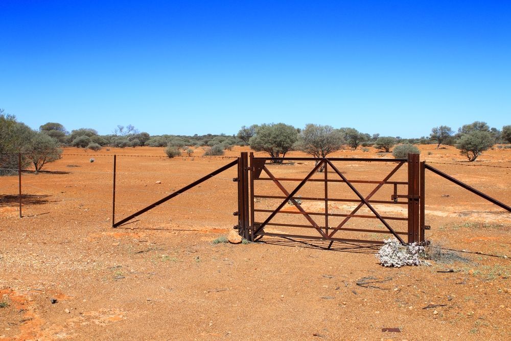 A Rusty Metal Gate in a Dry, Desert Landscape Under a Clear Blue Sky — Milton Electrical Projects In Kaban, QLD
