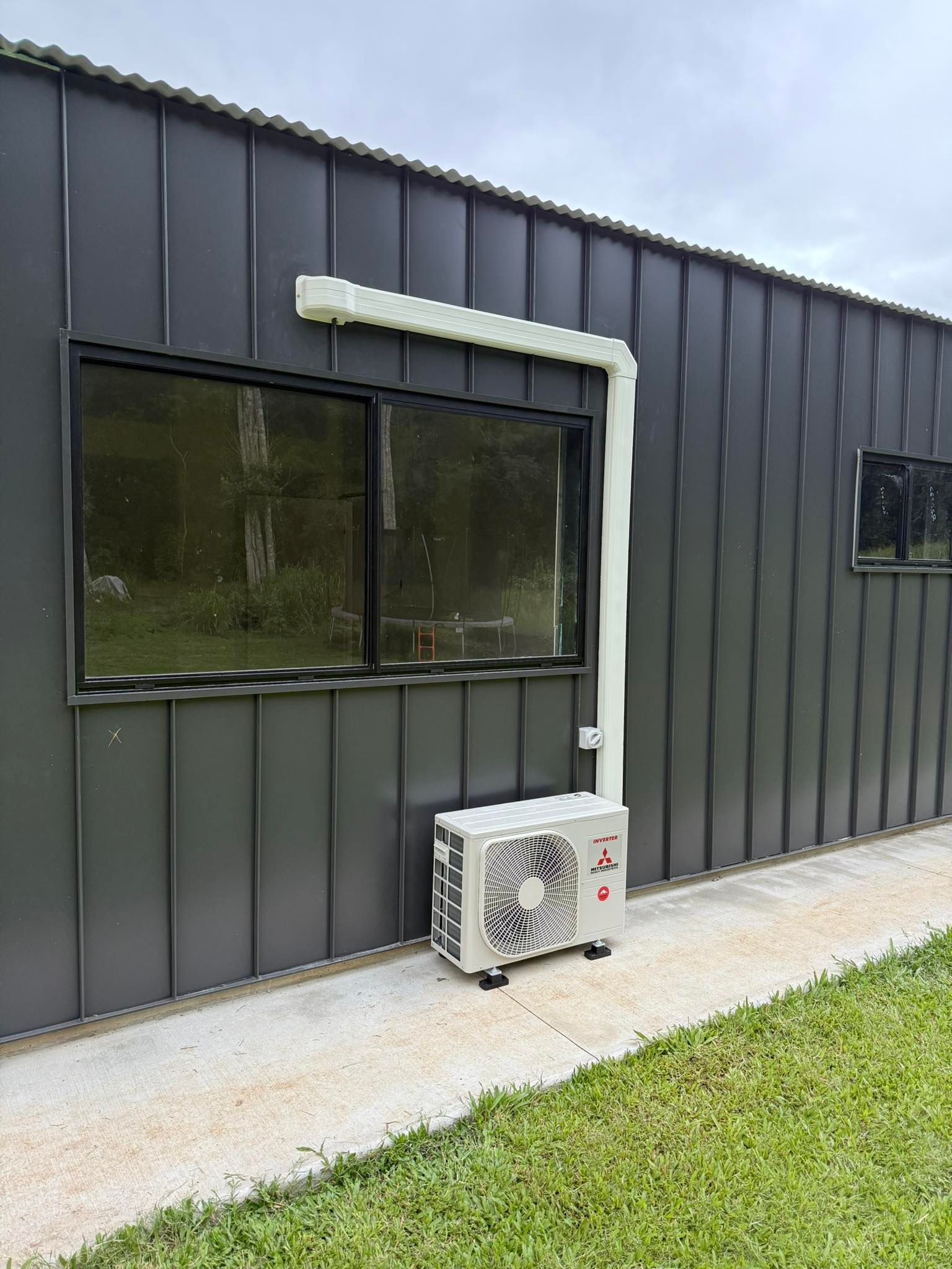 An Air Conditioning Unit on a Dark Gray Building's Exterior, With White Ducting — Milton Electrical Projects in Kaban, QLD