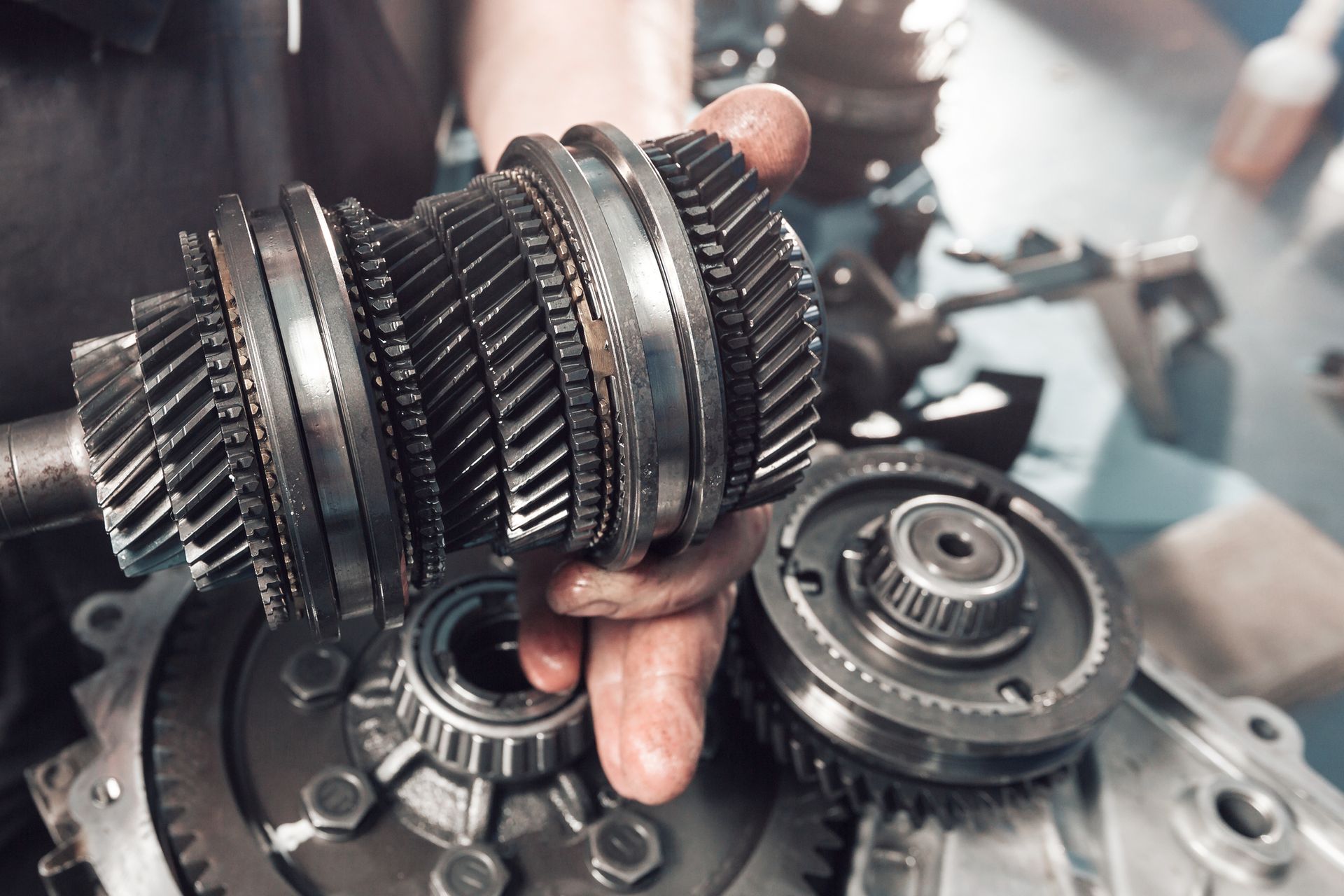 Close-up of a hand holding gears from a vehicle transmission, showing intricate metal parts in a repair setting.