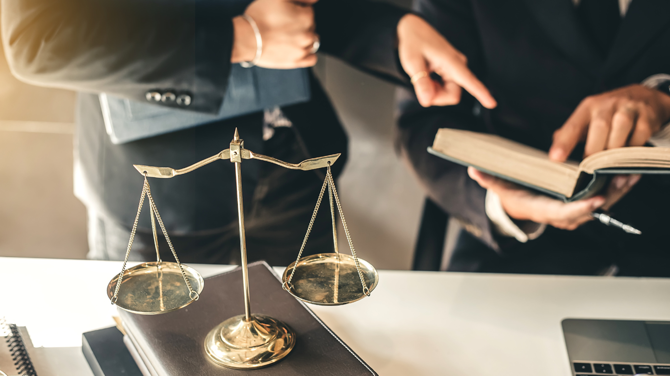 A group of people are standing around a table with a scale of justice and a book.