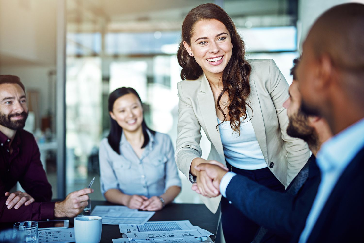 A group of people are sitting around a table shaking hands.