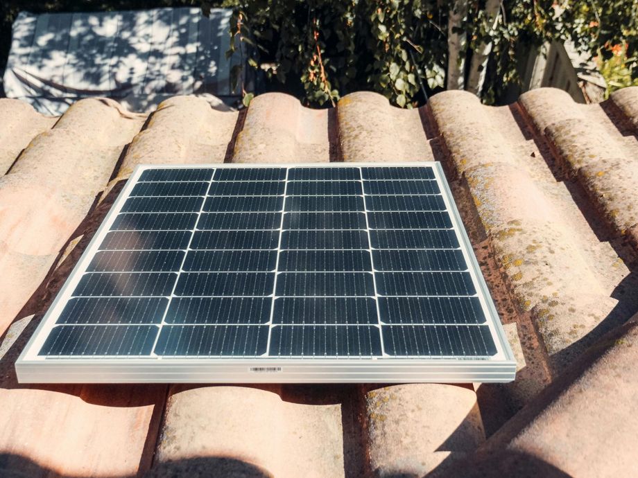 Solar panel resting on a terracotta tile roof under sunlight. The panel is black and framed in silver.