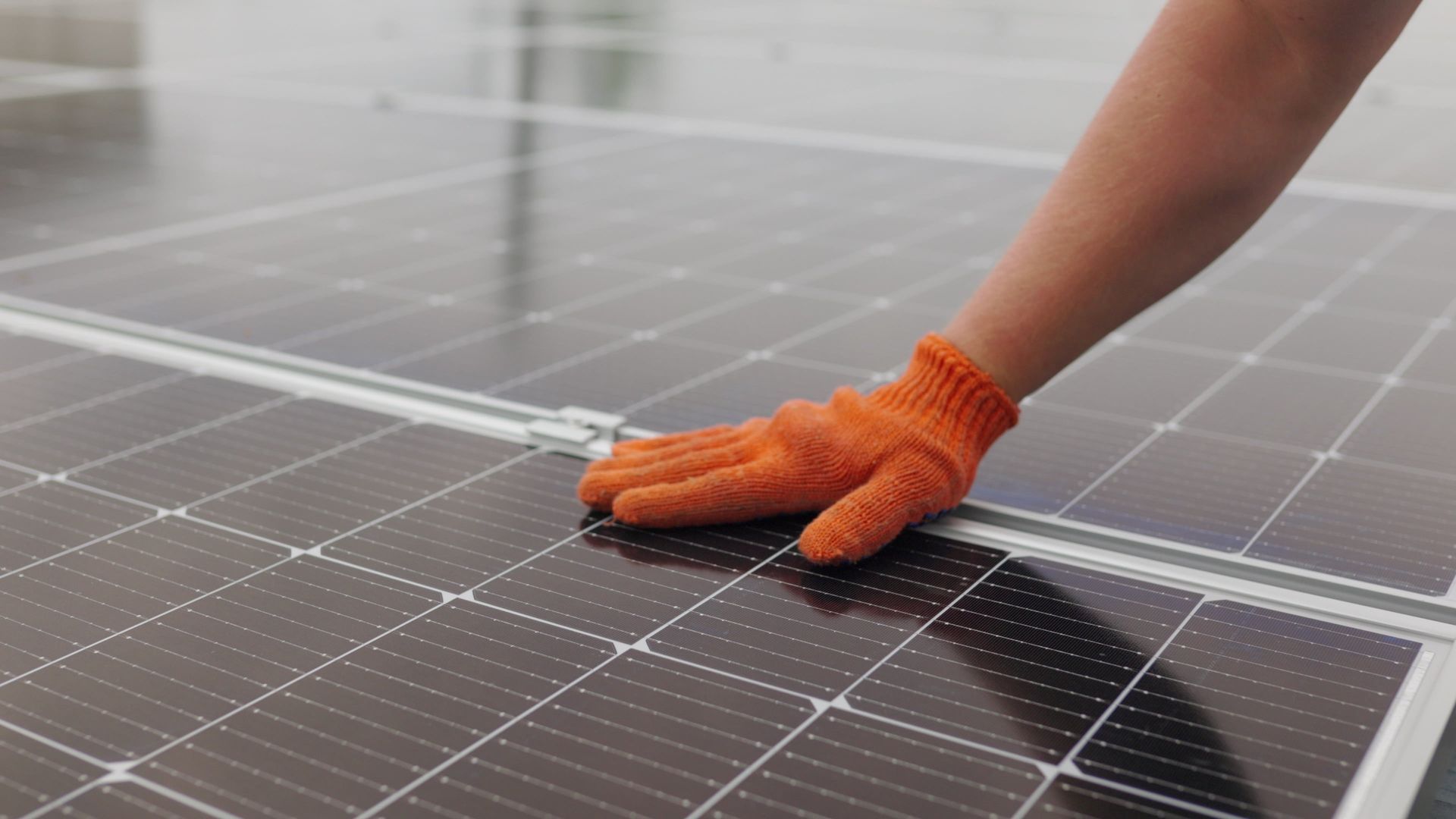 Hand wearing orange work glove touching a solar panel array on a rooftop.