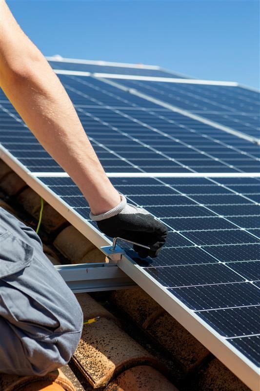 Solar panel installation: worker in gloves secures a solar panel on a rooftop, with bright blue sky in the background.