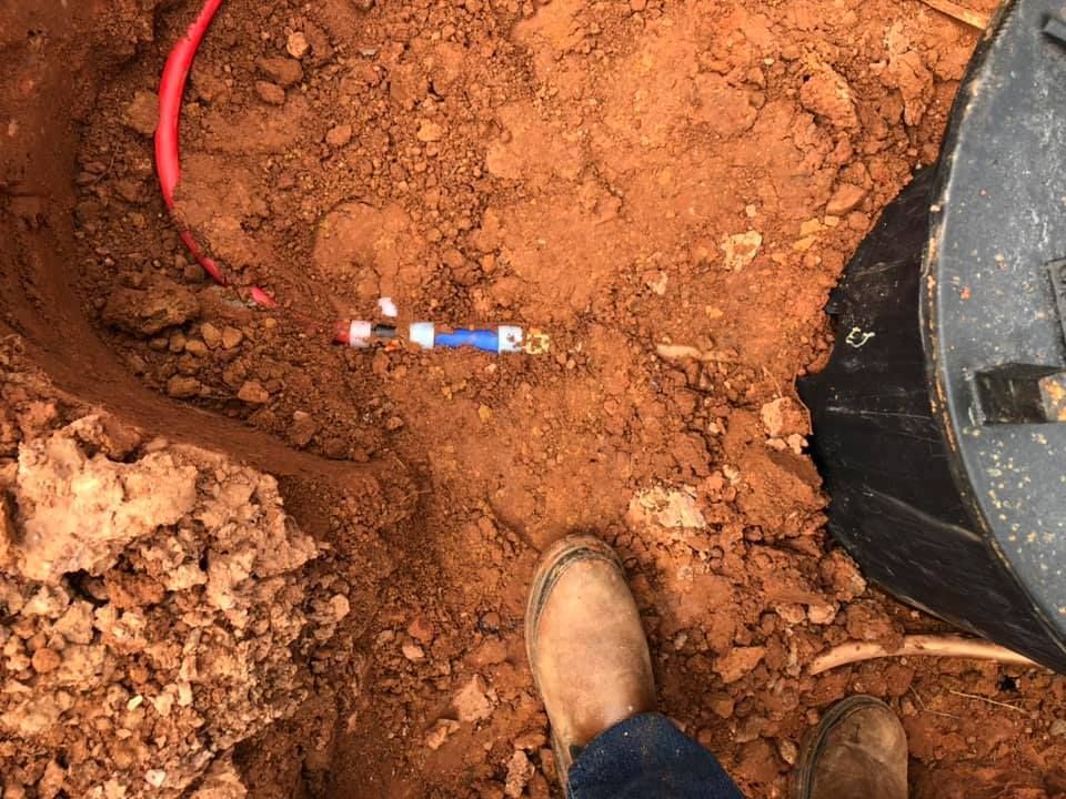 Person's boots in a dirt trench, near red wire and a white and blue object.