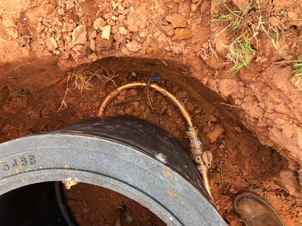 Open access port with copper piping and fittings in an earthen trench.