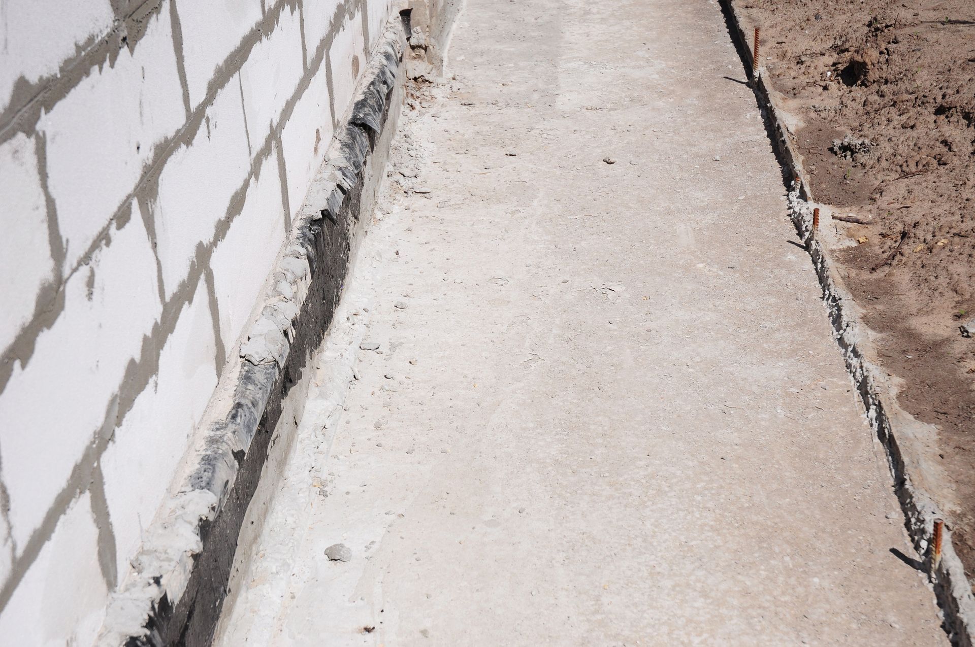 Concrete pathway alongside a white brick wall and brown soil.