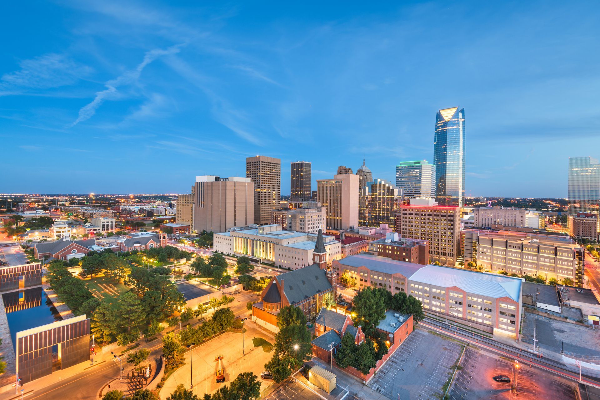 Downtown Oklahoma City skyline at dusk with blue sky and lit buildings.