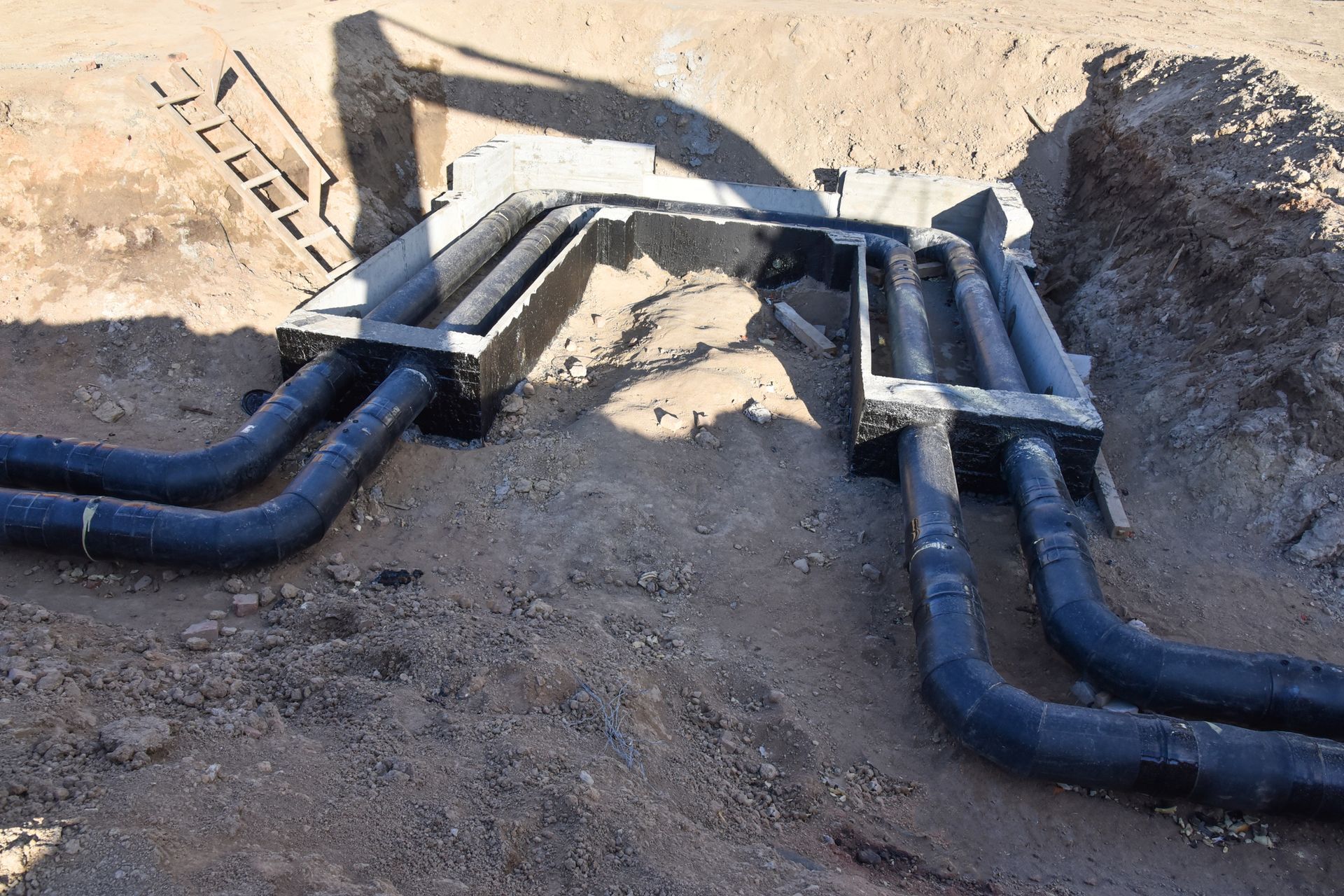 Black pipes running through a concrete structure in a dirt excavation.