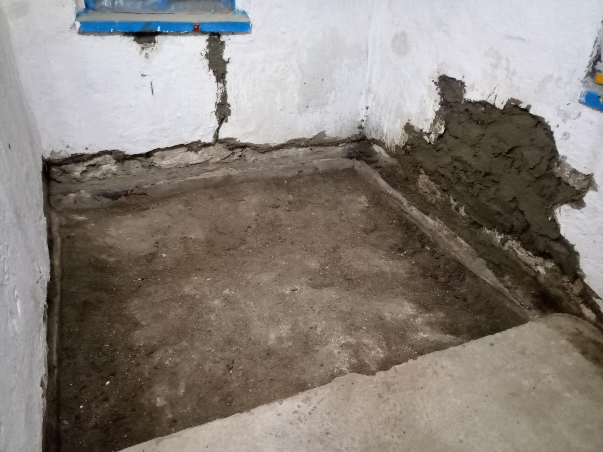 Concrete floor repair in a corner of a room, with wet cement patching walls and floor edges.