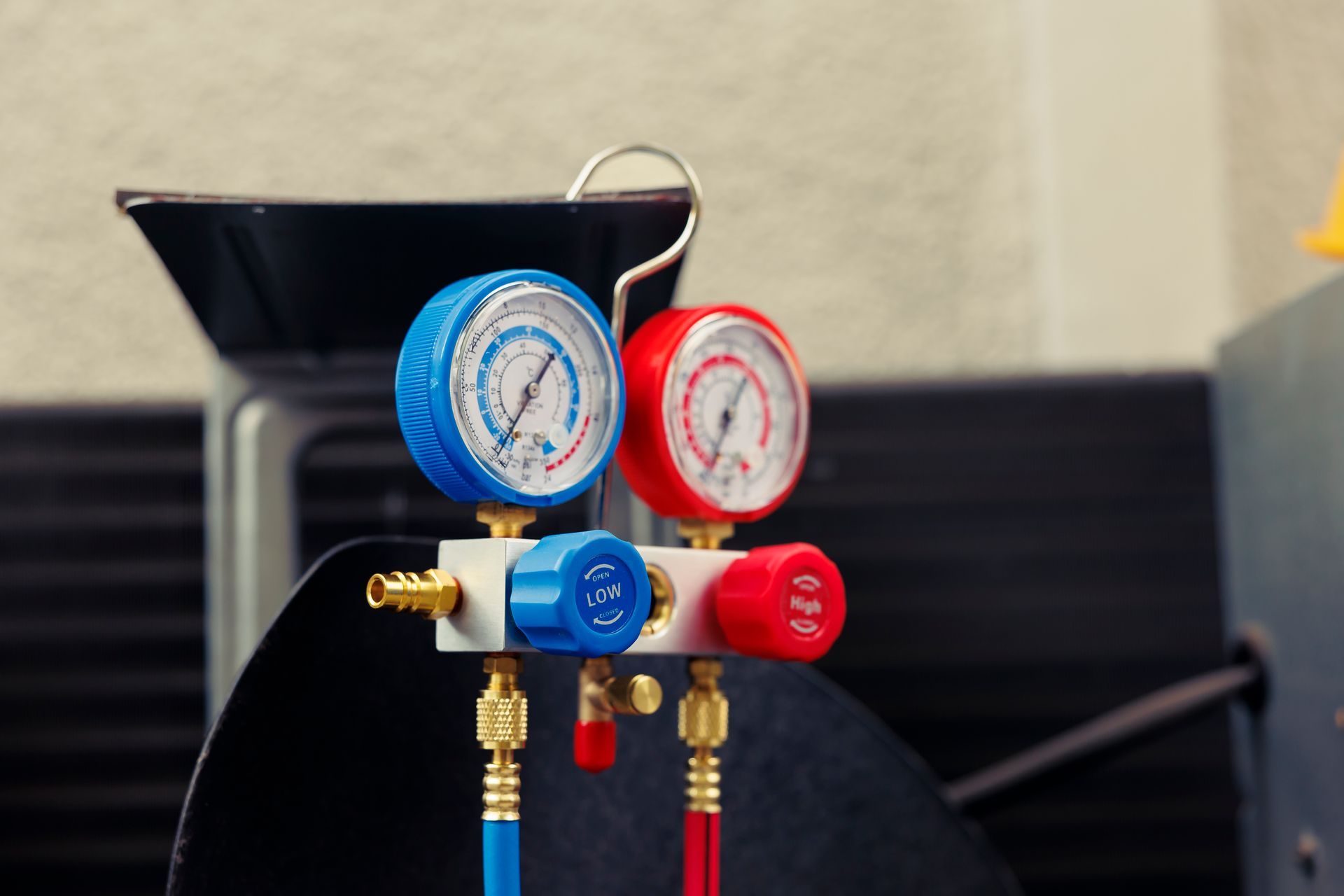 Close-up of a blue and red manifold gauge set for HVAC. Hoses connect to the set for measuring pressure.