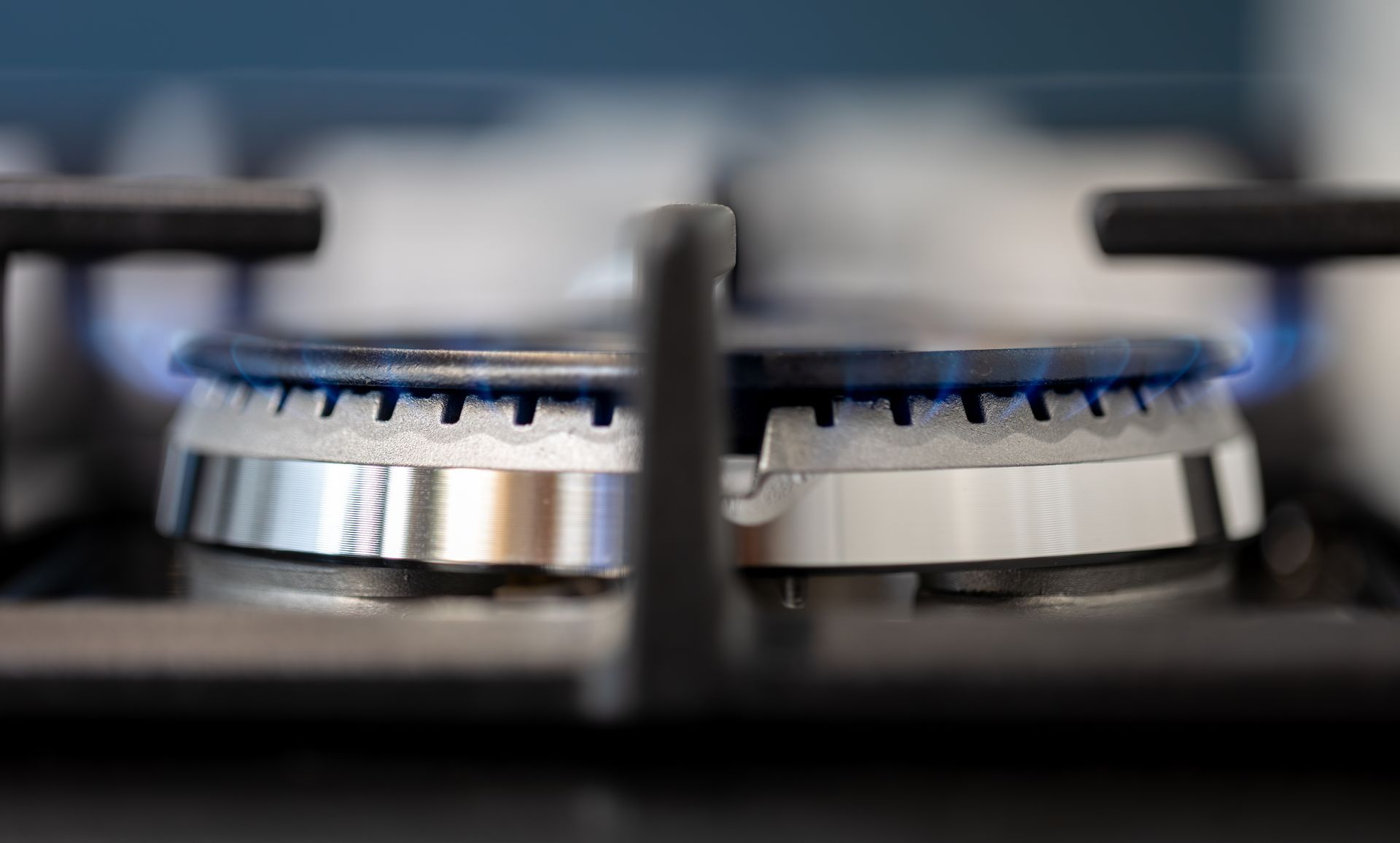 Close-up of a gas stove burner lit with a blue flame. Stainless steel and black stovetop.