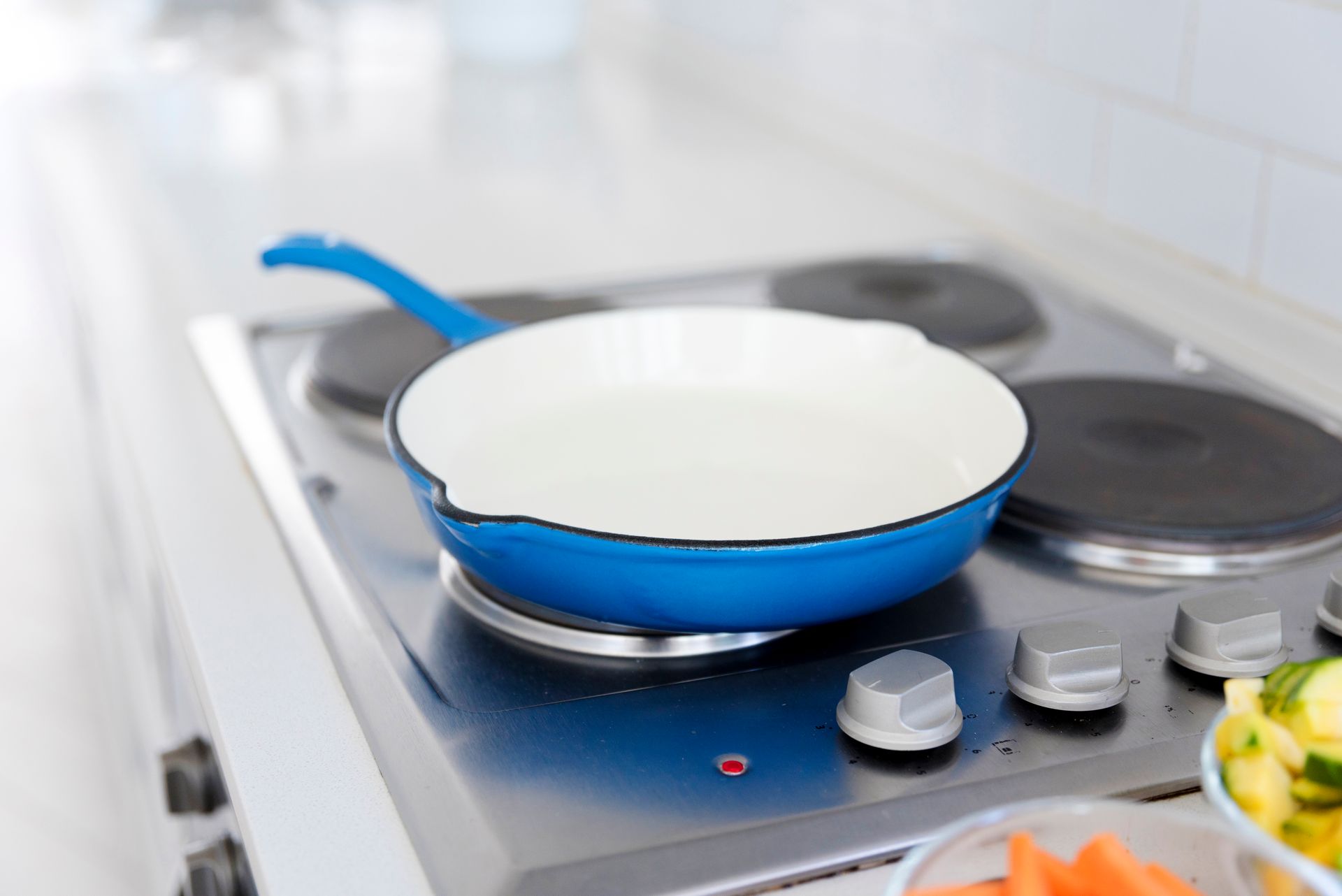 Blue and white frying pan on a stovetop, ready for cooking with vegetables in the foreground.