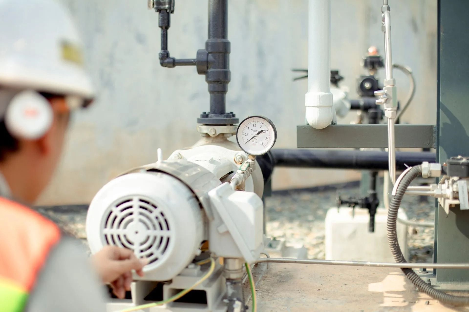 Person in hard hat inspecting machinery with a gauge.