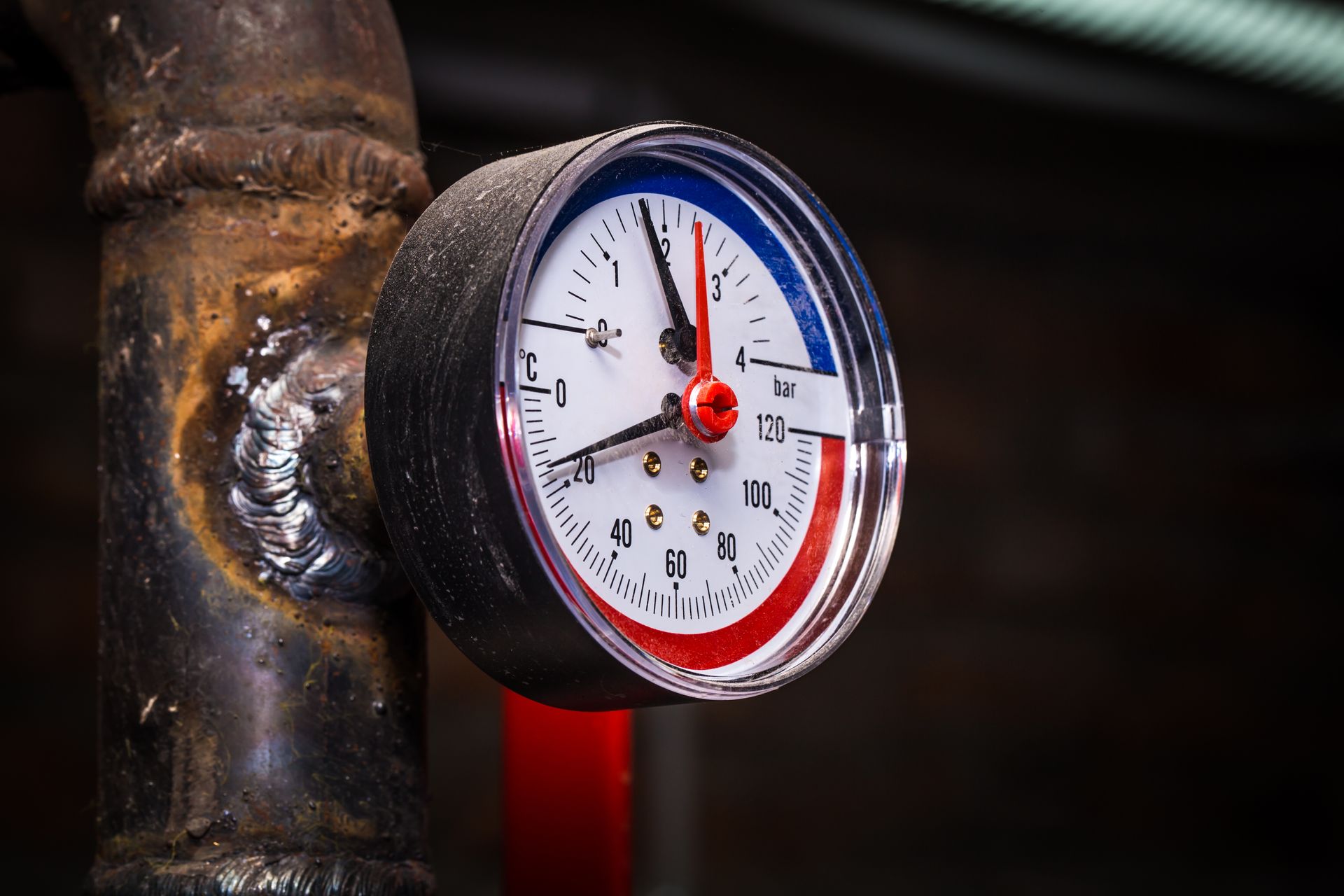 Pressure gauge on rusty pipe; needle indicates a normal range. Red and blue color-coded sections.