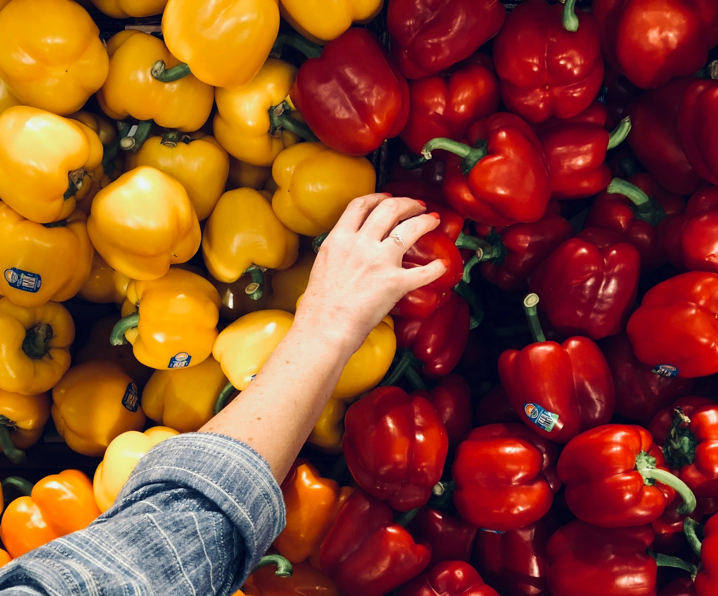 A person reaching out for red peppers.