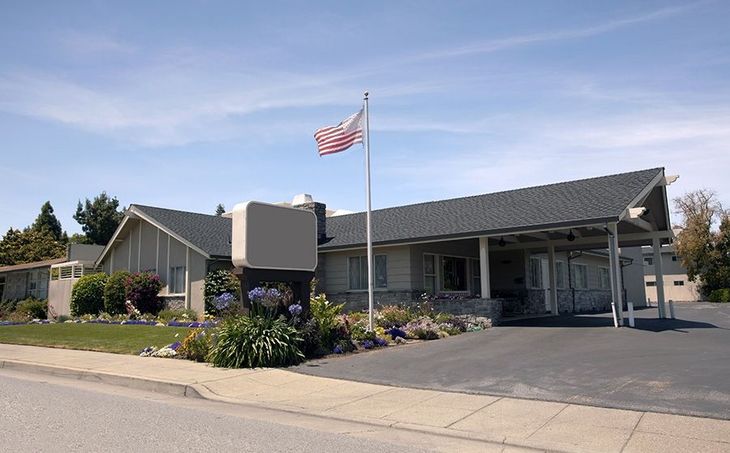 A light-colored building with an American flag, a sign, and a covered carport.
