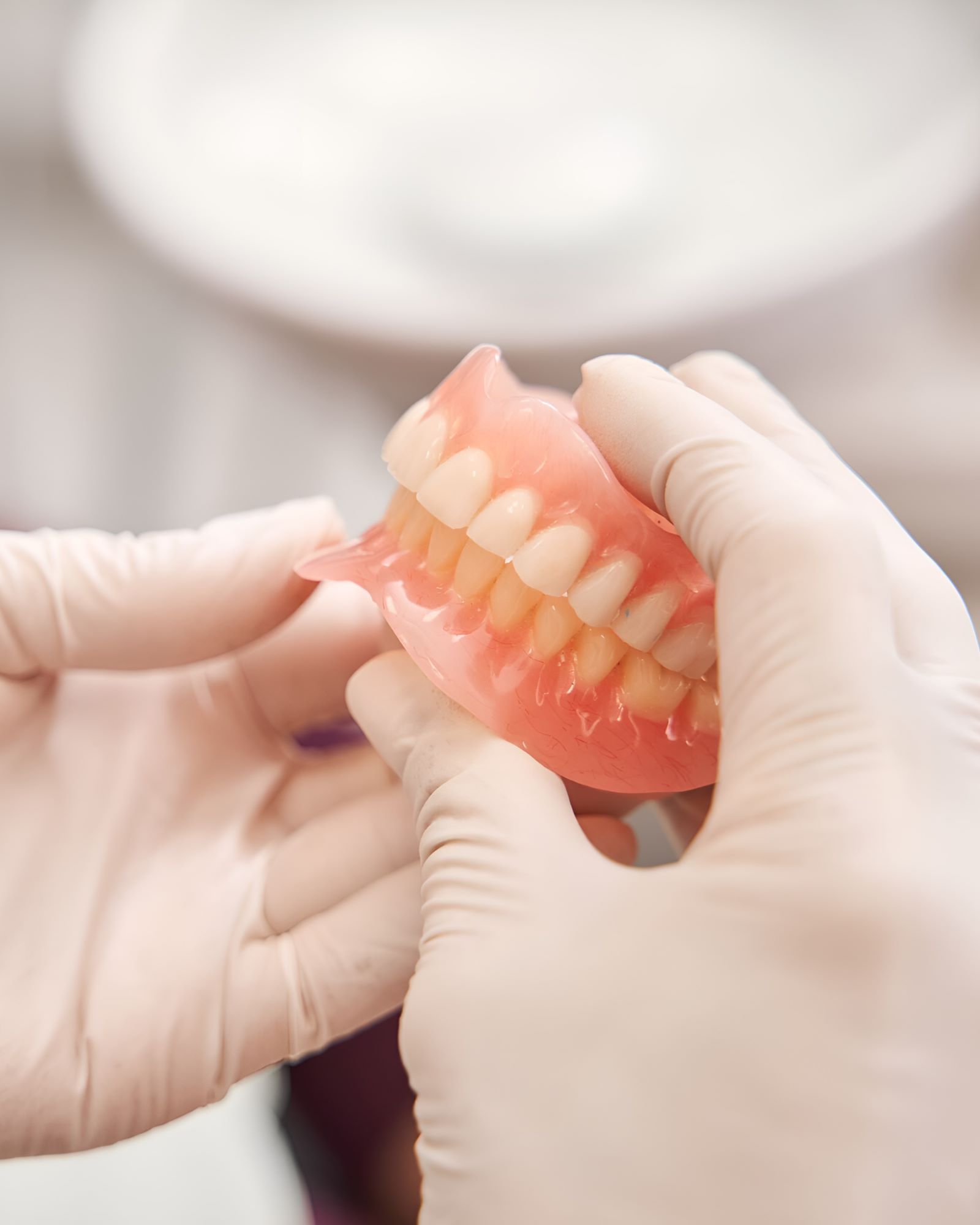 A Person Wearing Gloves is Holding a Denture in Their Hands — Yeppoon Denture Clinic in Gladstone, QLD