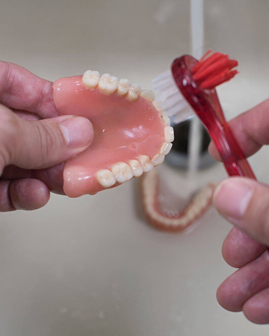 A Person is Cleaning a Denture With a Toothbrush — Yeppoon Denture Clinic in Taranganba, QLD