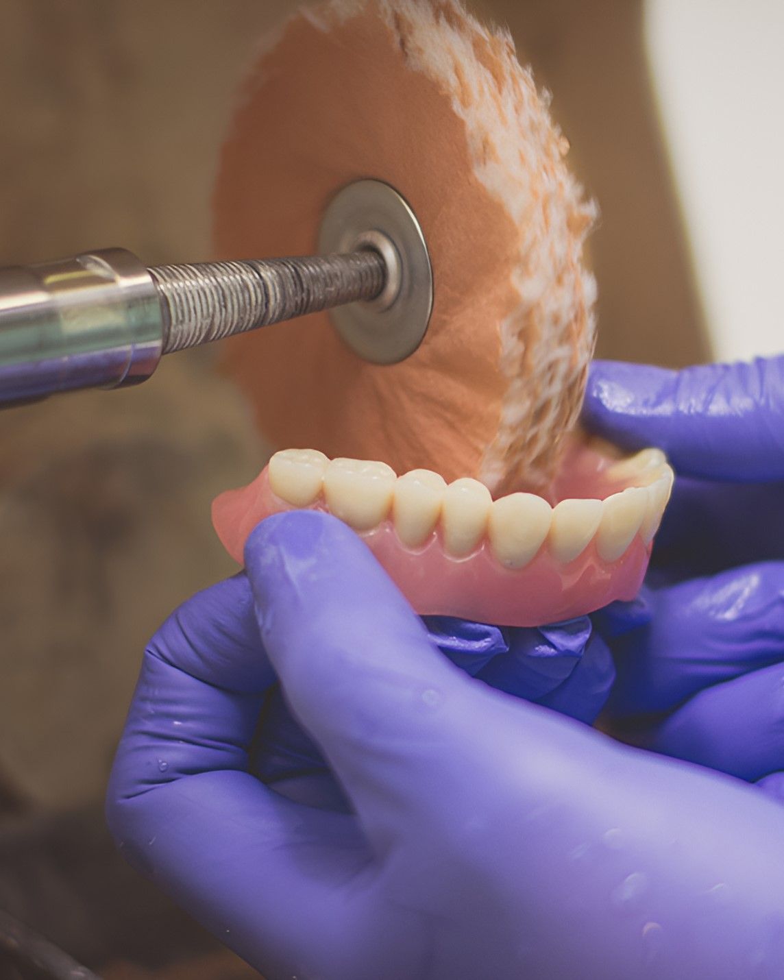 A Person Wearing Blue Gloves is Polishing a Denture With a Machine — Yeppoon Denture Clinic in Gladstone, QLD