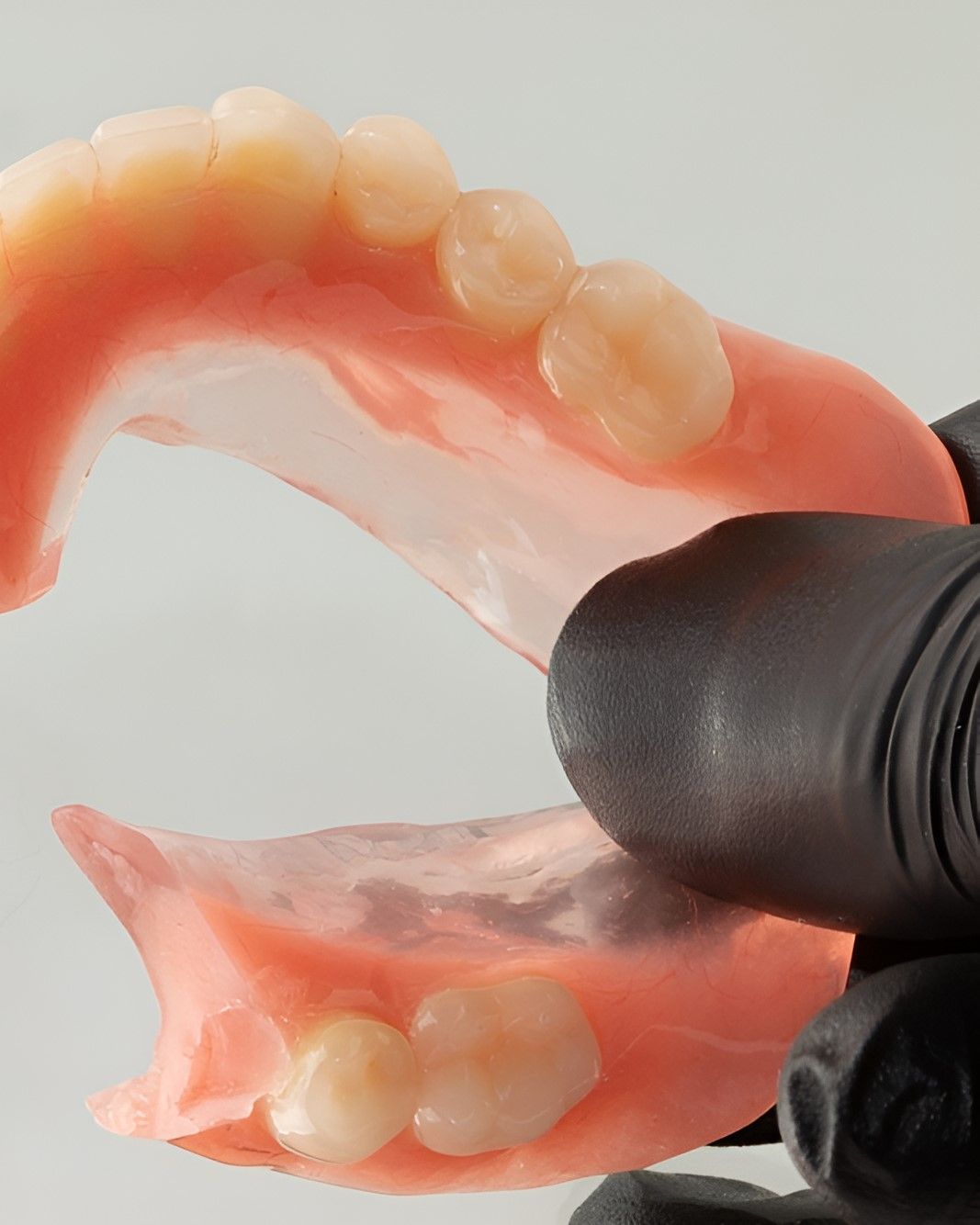 A Person Wearing Black Gloves is Holding a Denture in Their Hand — Yeppoon Denture Clinic in Taranganba, QLD