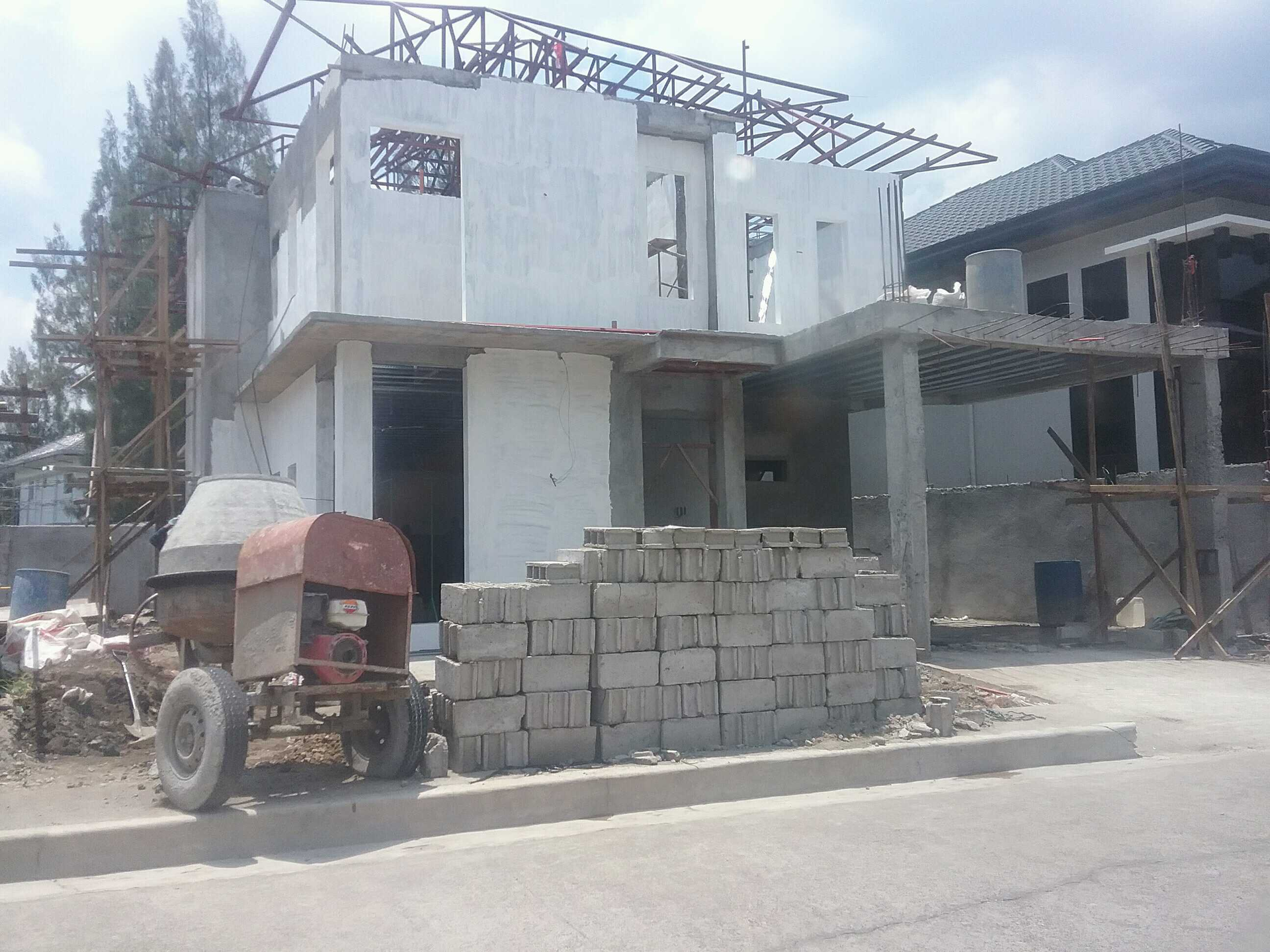 Two-story house with a white deck, parked cars, and a road in a town. Overcast sky.