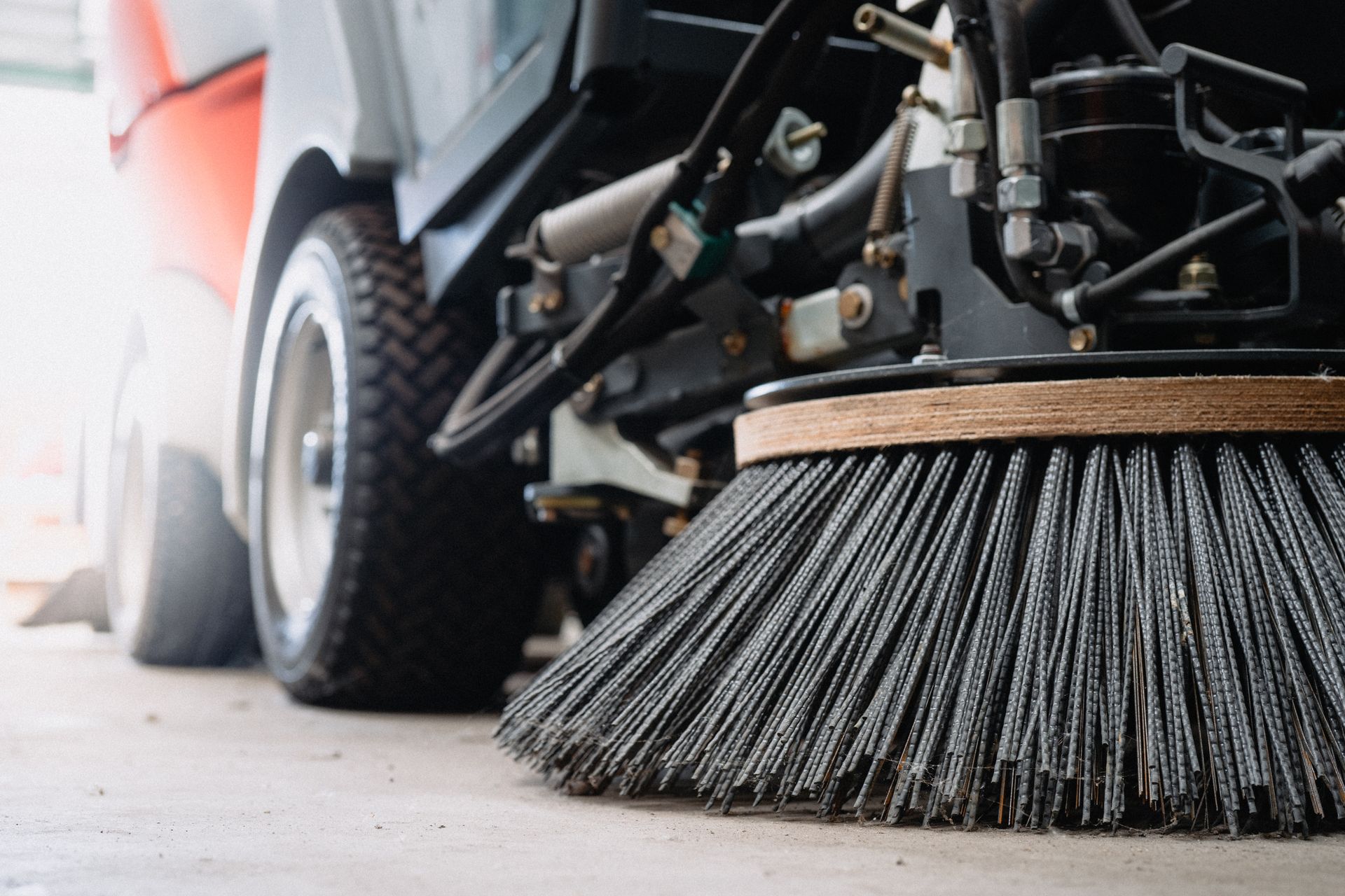 Close-up of a commercial sweeping services machine using a rotating brush to clean pavement.