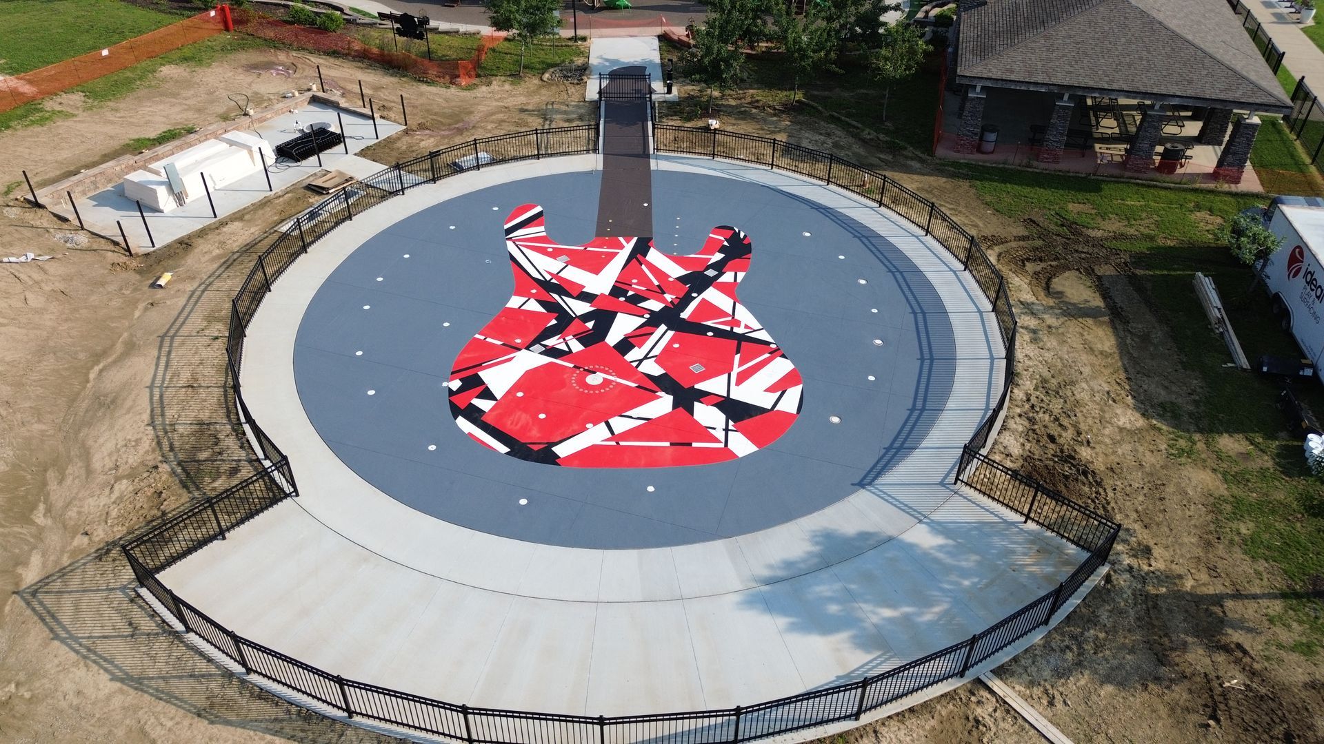 Aerial view of a gray guitar-shaped memorial with red and white patterns, surrounded by a circular platform.