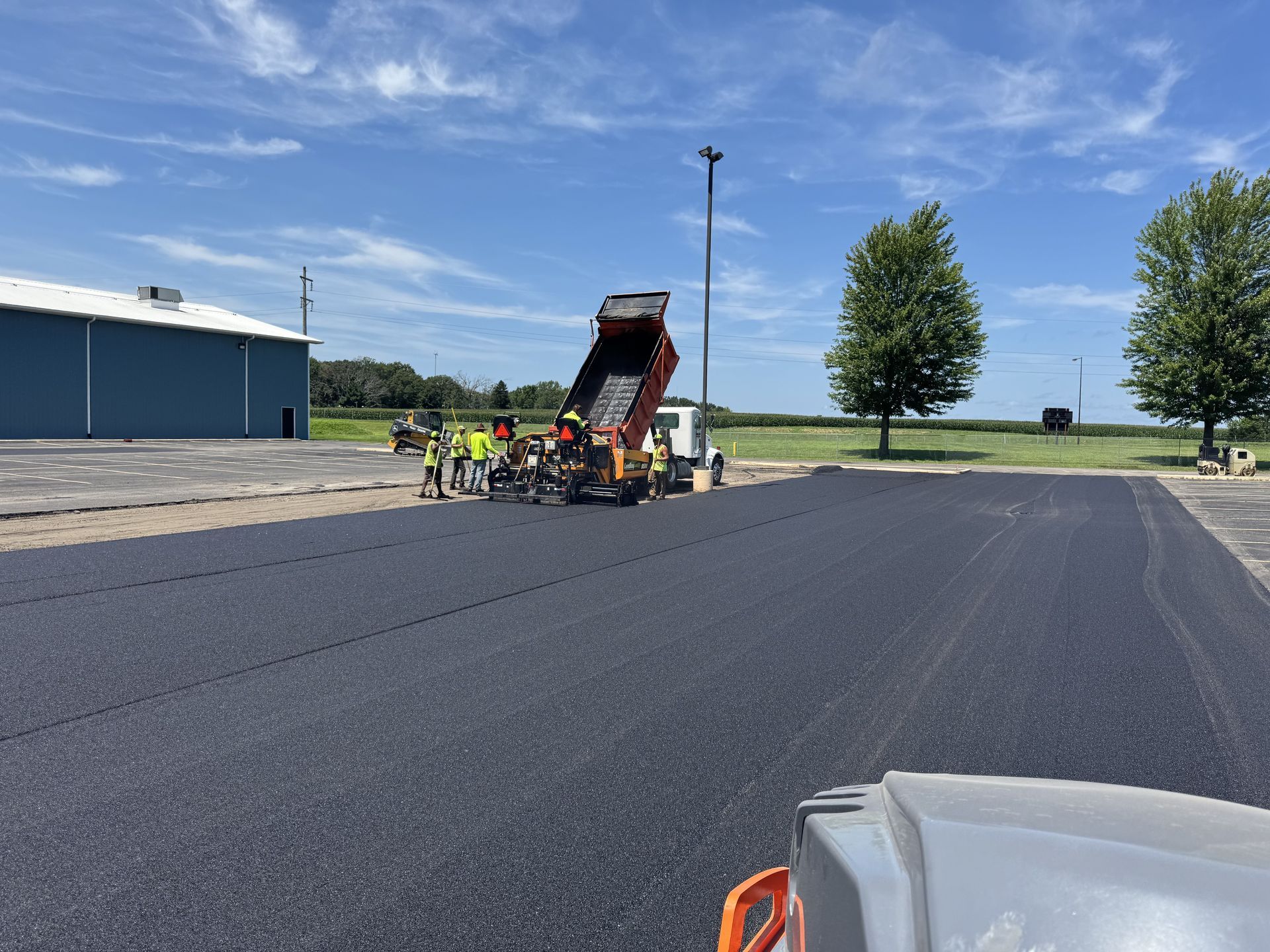 Asphalt paving in progress: truck dumping asphalt into a paving machine on a sunny day.