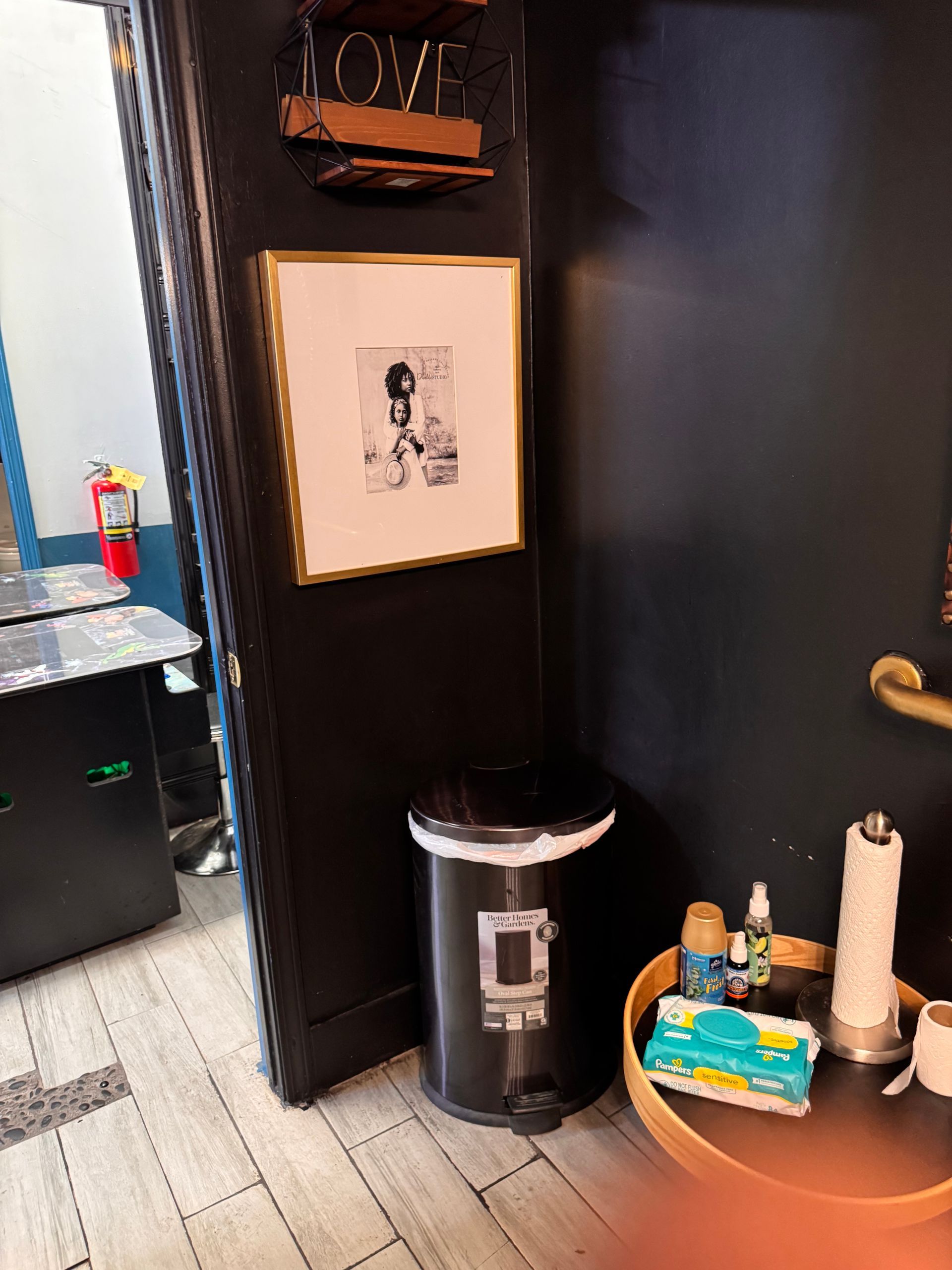 A bathroom with a trash can and a picture on the wall that says love