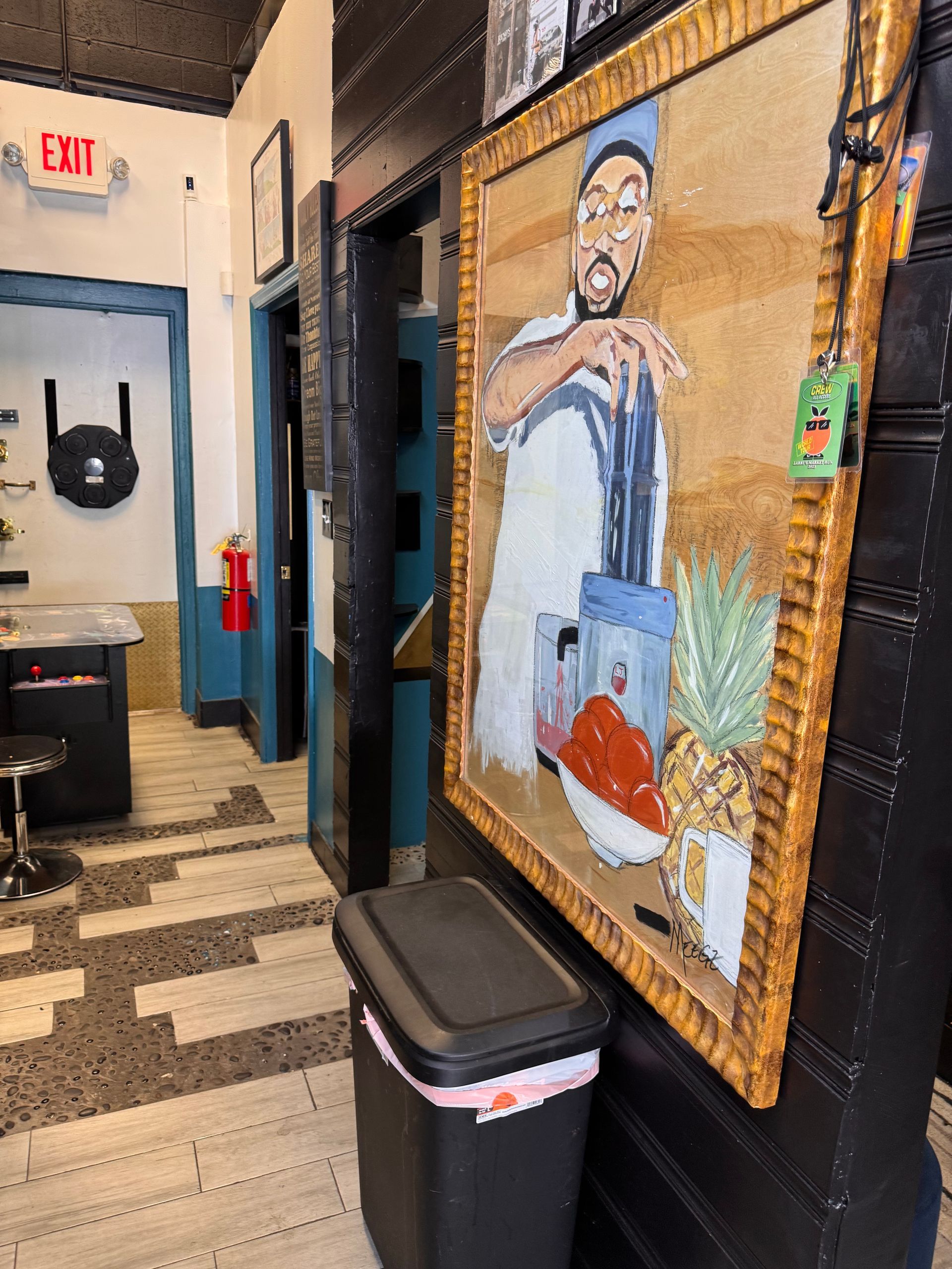 A painting of a chef is hanging on a wall next to a trash can.