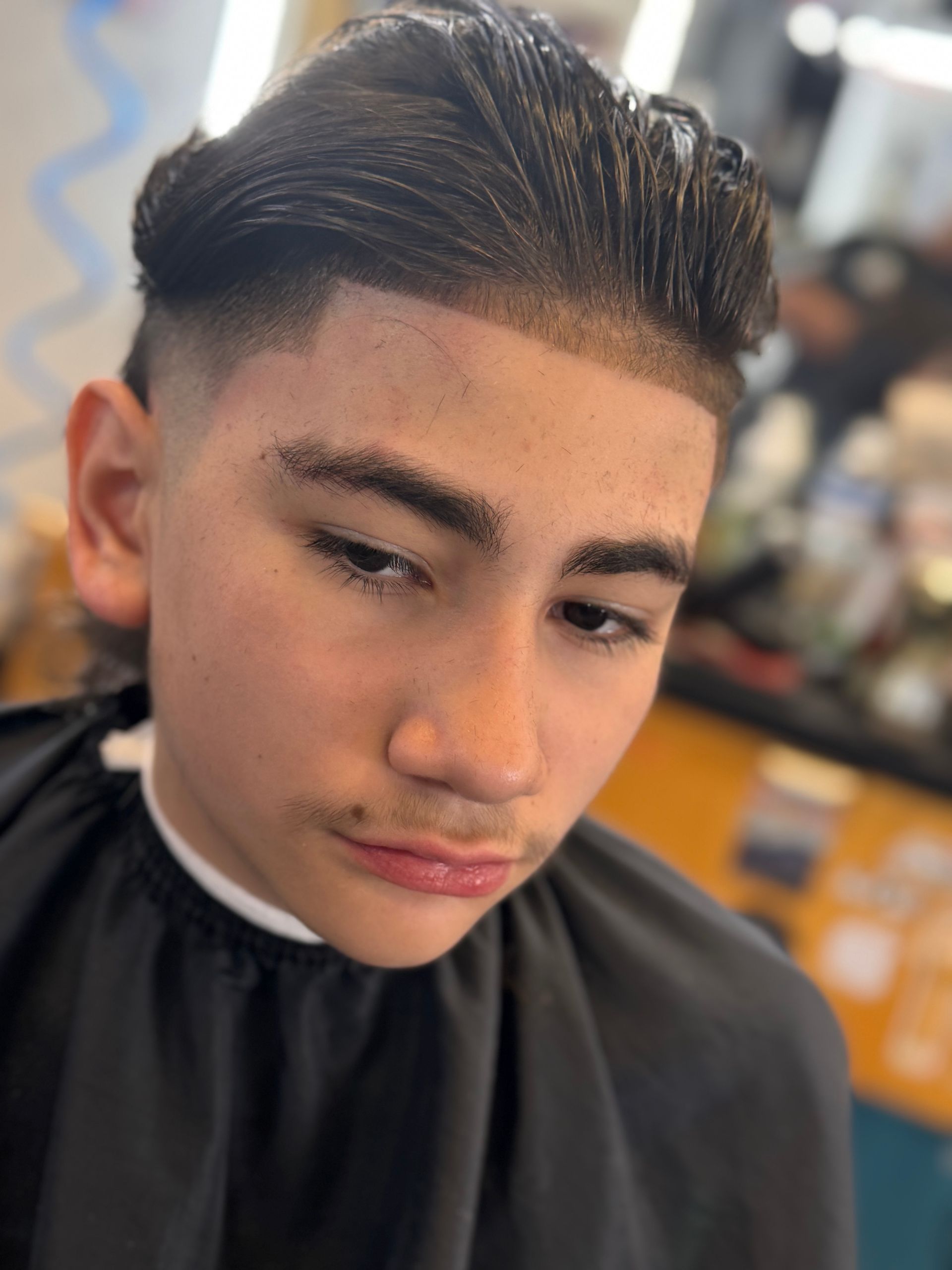 A young man is getting his hair cut at a barber shop.
