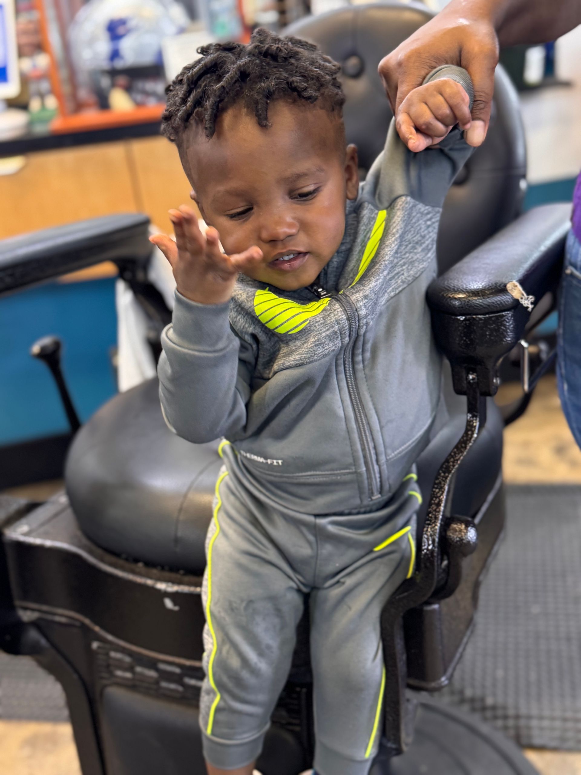 A little boy is sitting in a barber chair holding someone 's hand.
