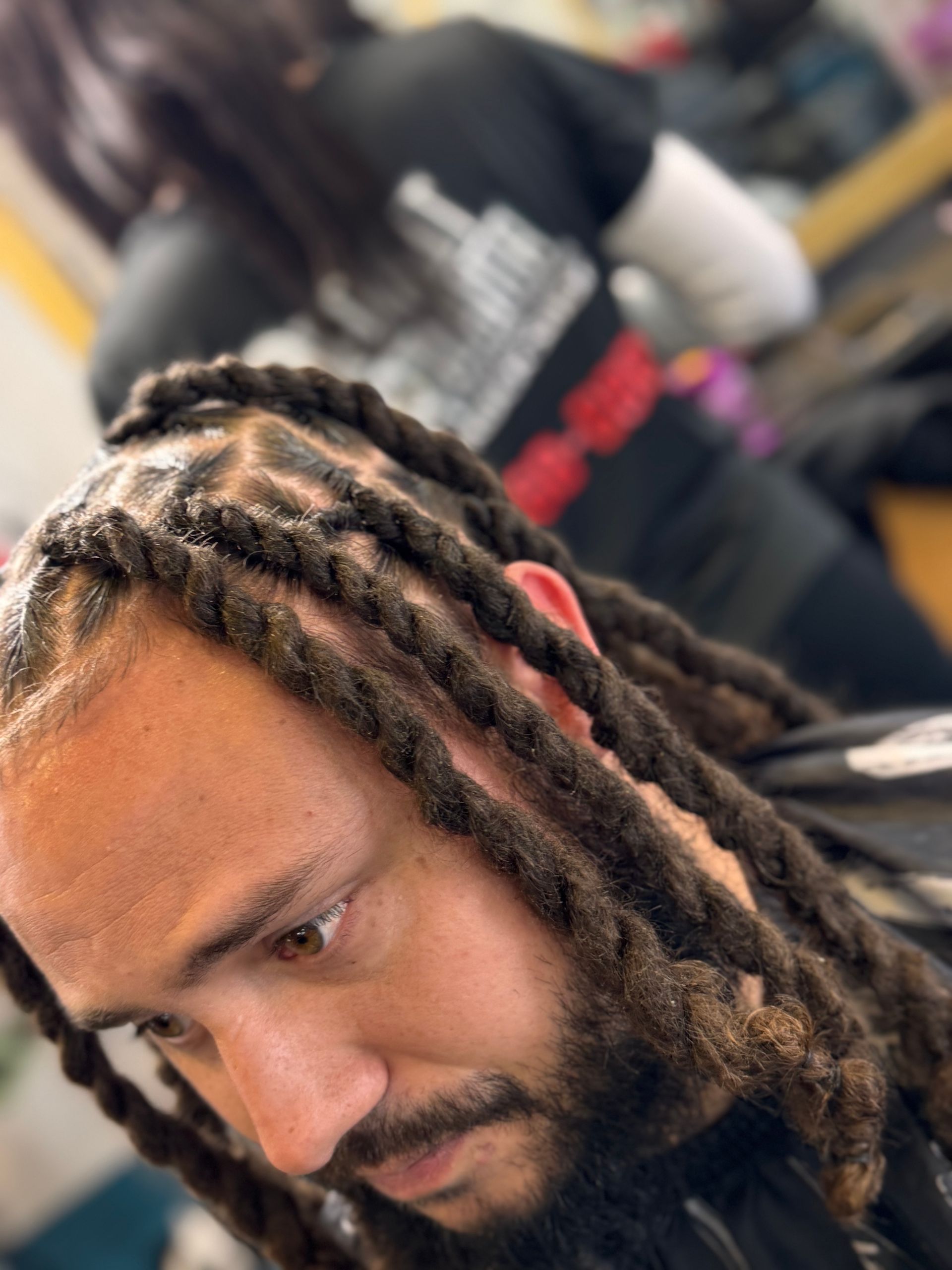 A man with dreadlocks and a beard is getting his hair cut in a salon.