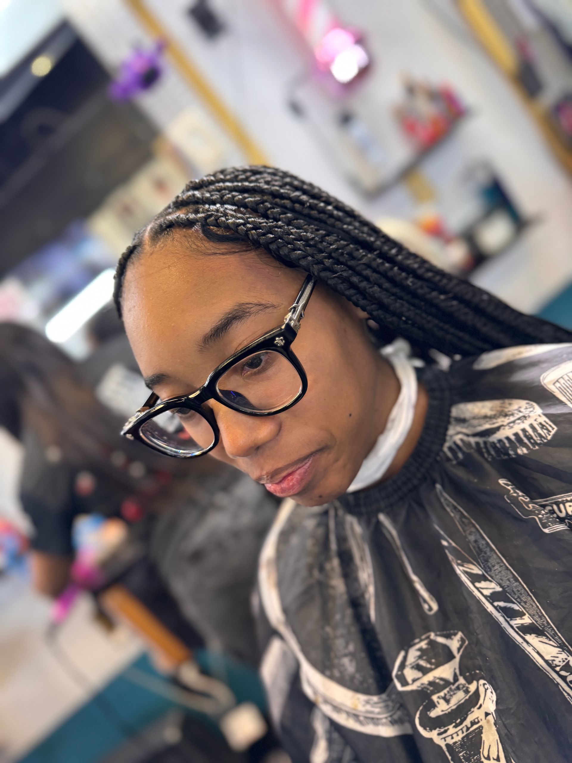 A woman wearing glasses is getting her hair braided in a salon.