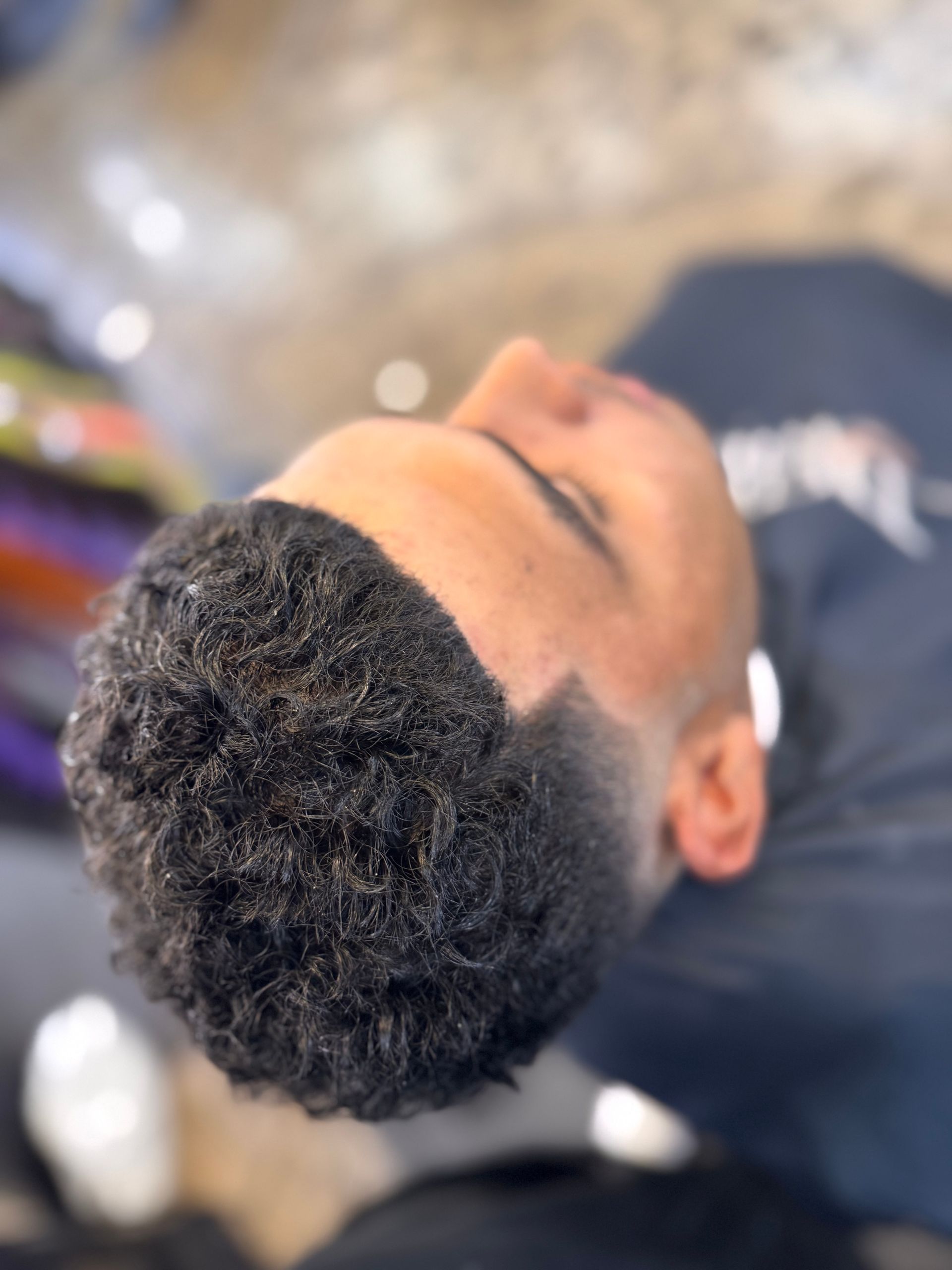 A man with curly hair is laying down with his eyes closed.